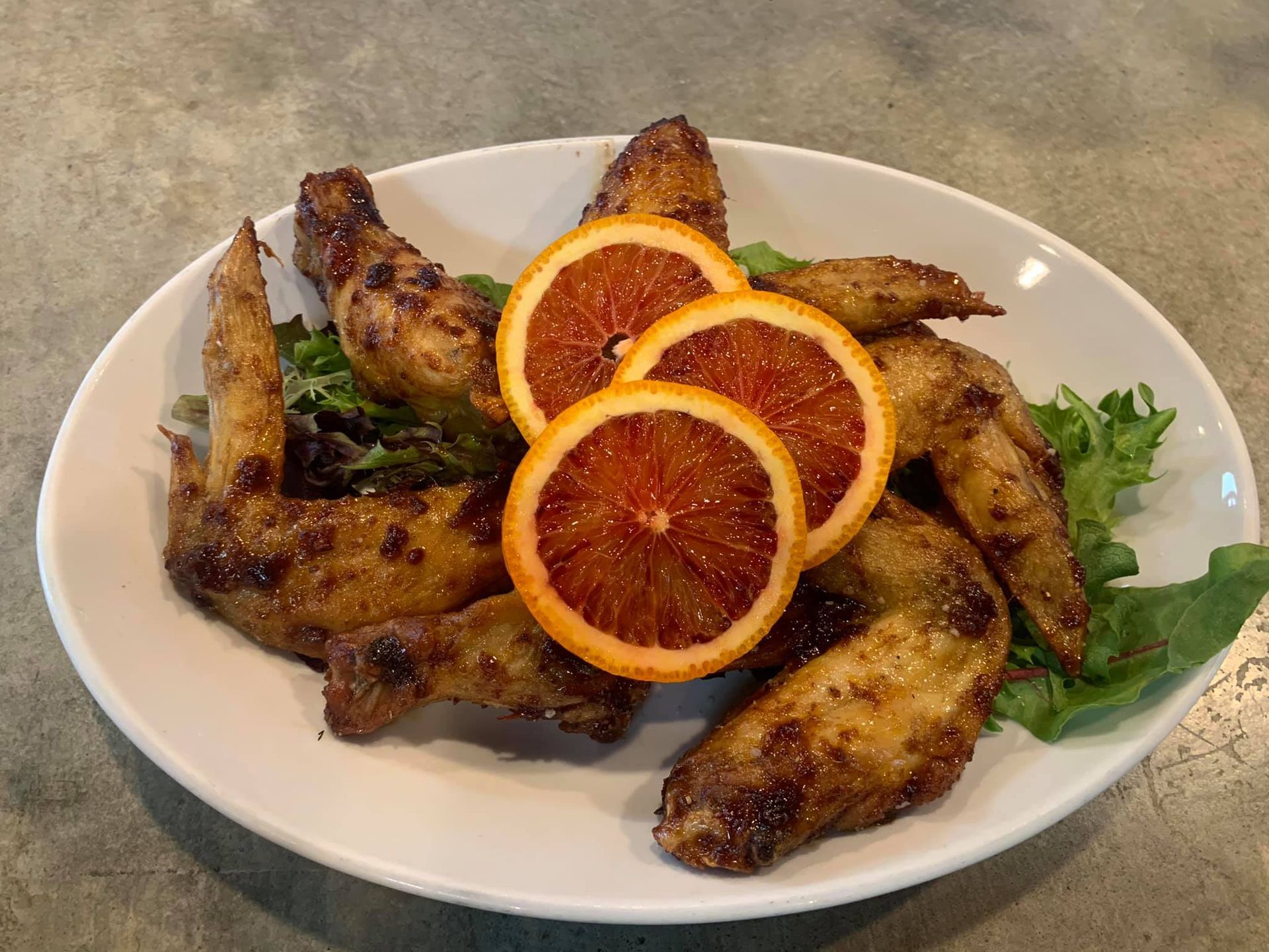 A white plate topped with chicken wings and orange slices.