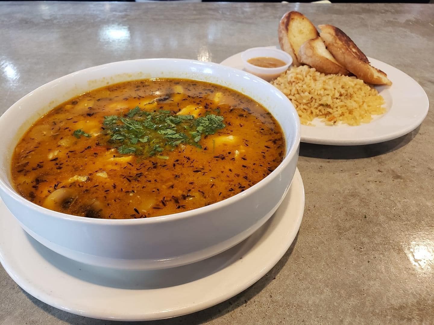 A bowl of soup and a plate of rice on a table.