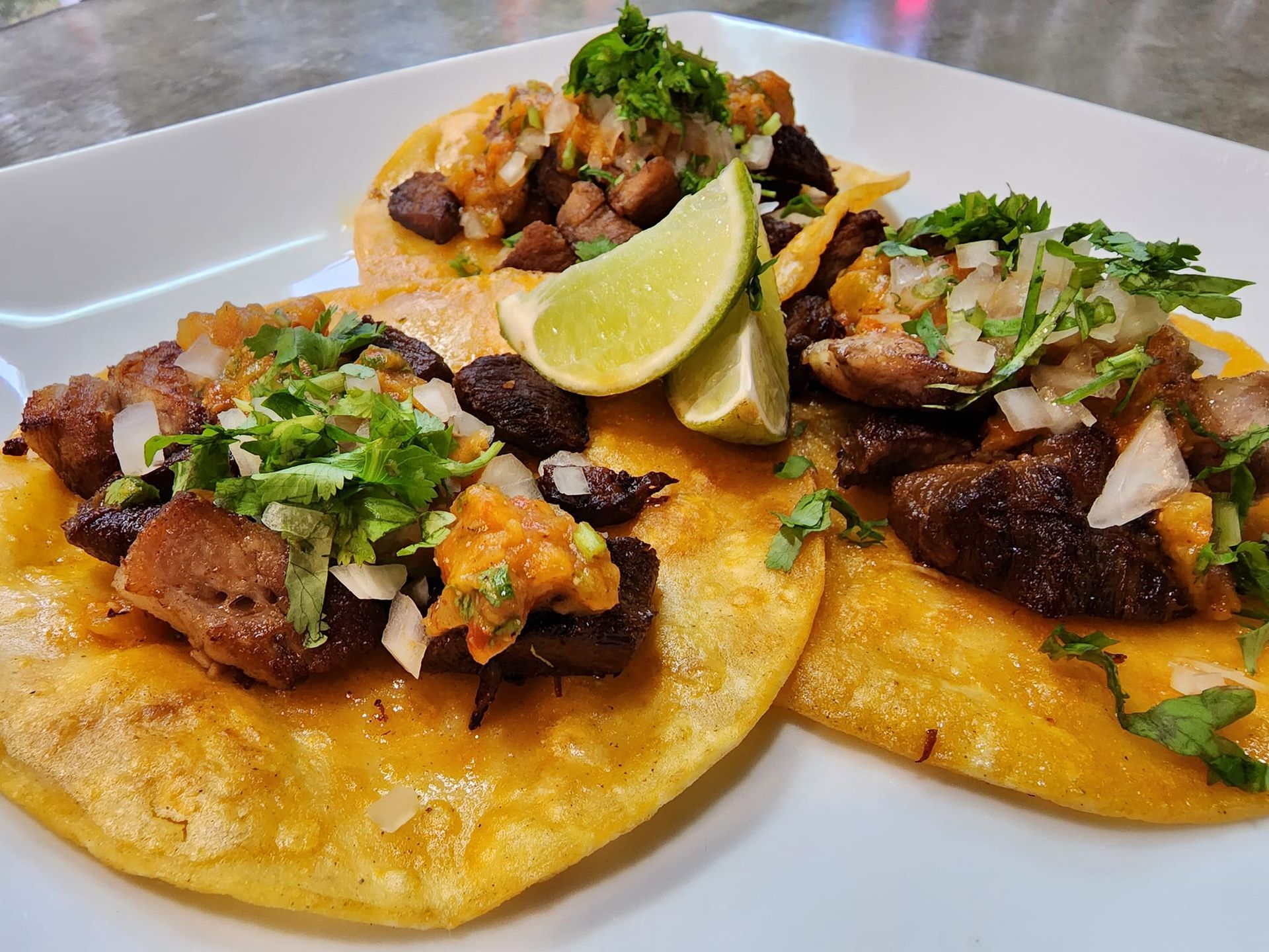 Three tacos with meat and vegetables on a white plate.