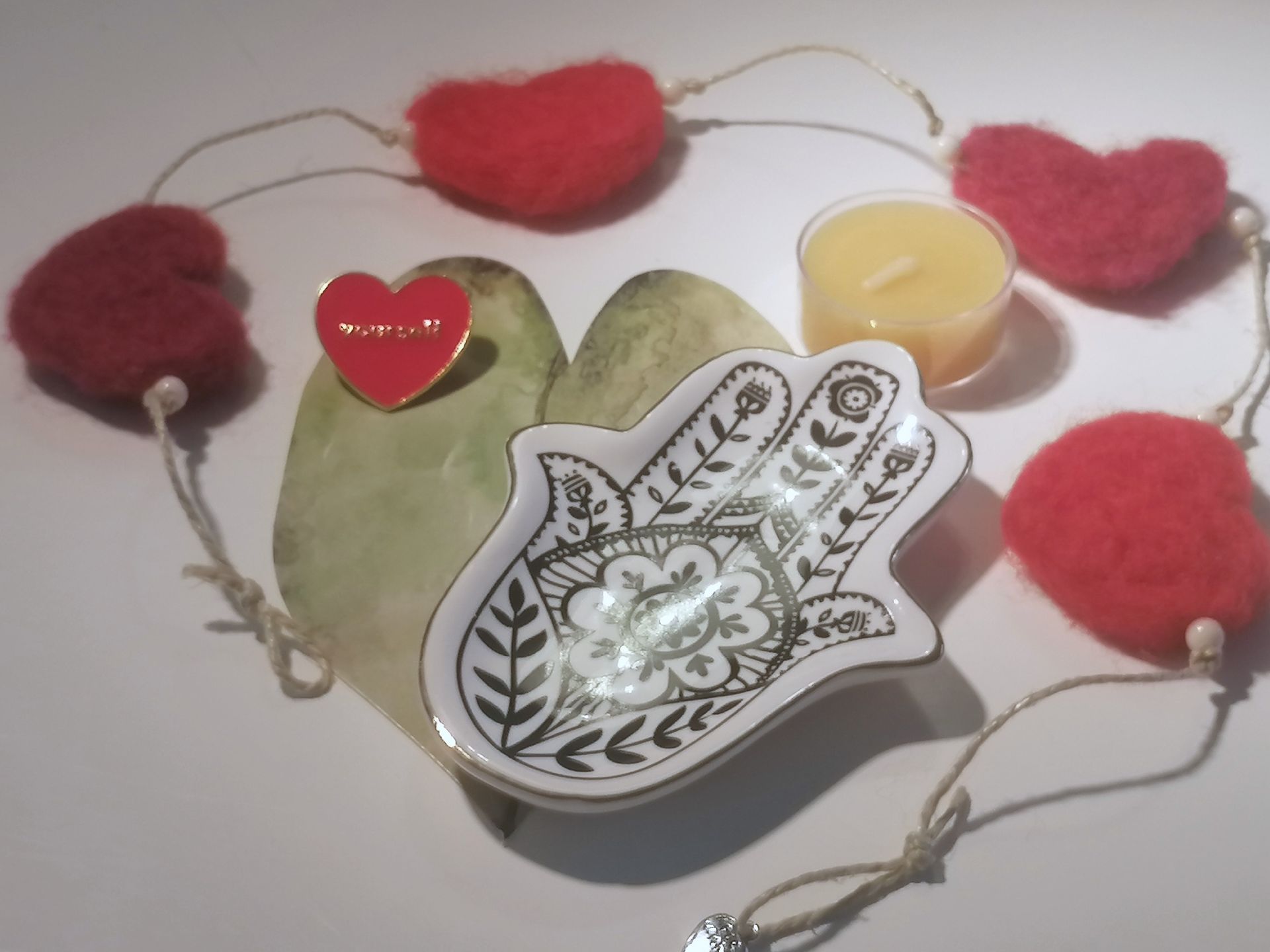 Hartvormige slinger, Hamsa-handschaaltje, rode hartspeld op een steen en een bijenwaskaarsje.