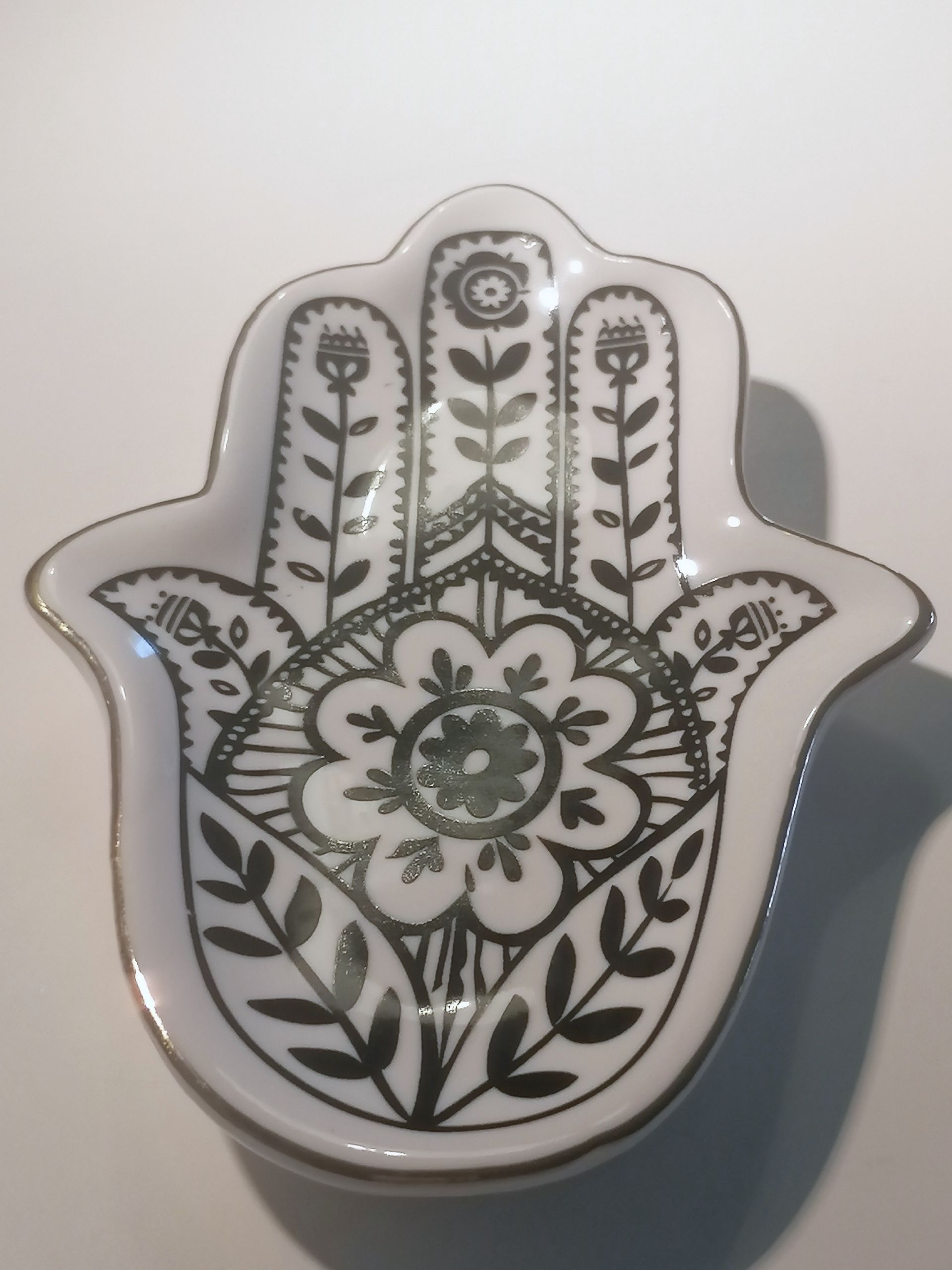 Wit keramieken sieradenschaaltje in de vorm van een Hamsa-hand, met zwart bloemenmotief en gouden rand.