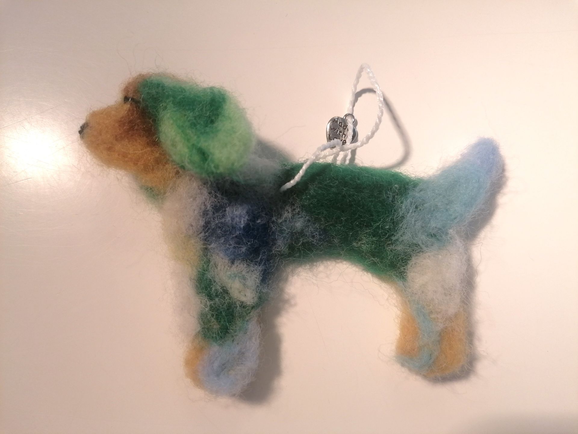 Hondenornament van vilt, gemaakt van groene, blauwe en gele wol, hangend aan een garen lus.