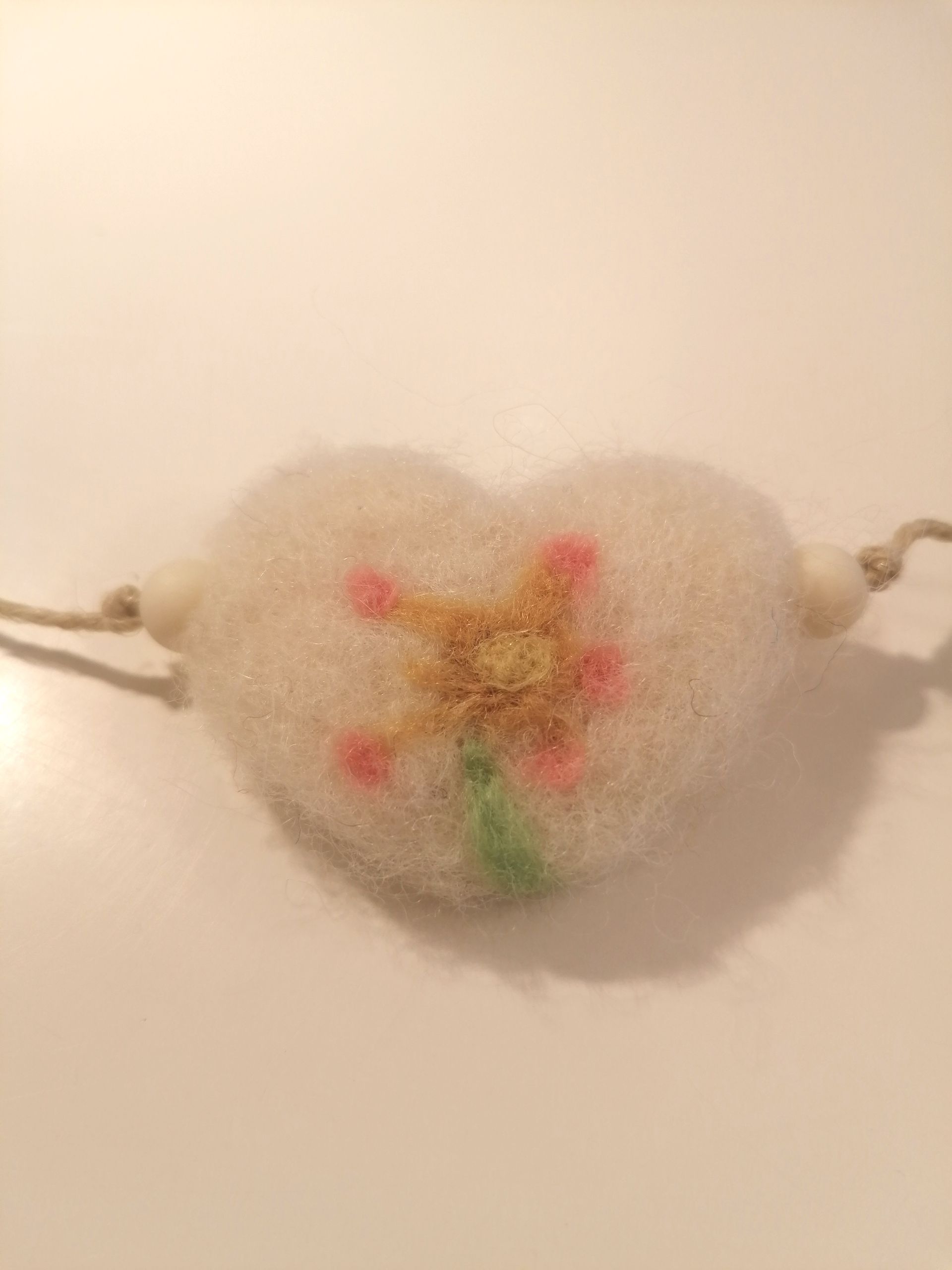 Hanger van wit wol in de vorm van een hart met een bloem, met touwtje eraan.