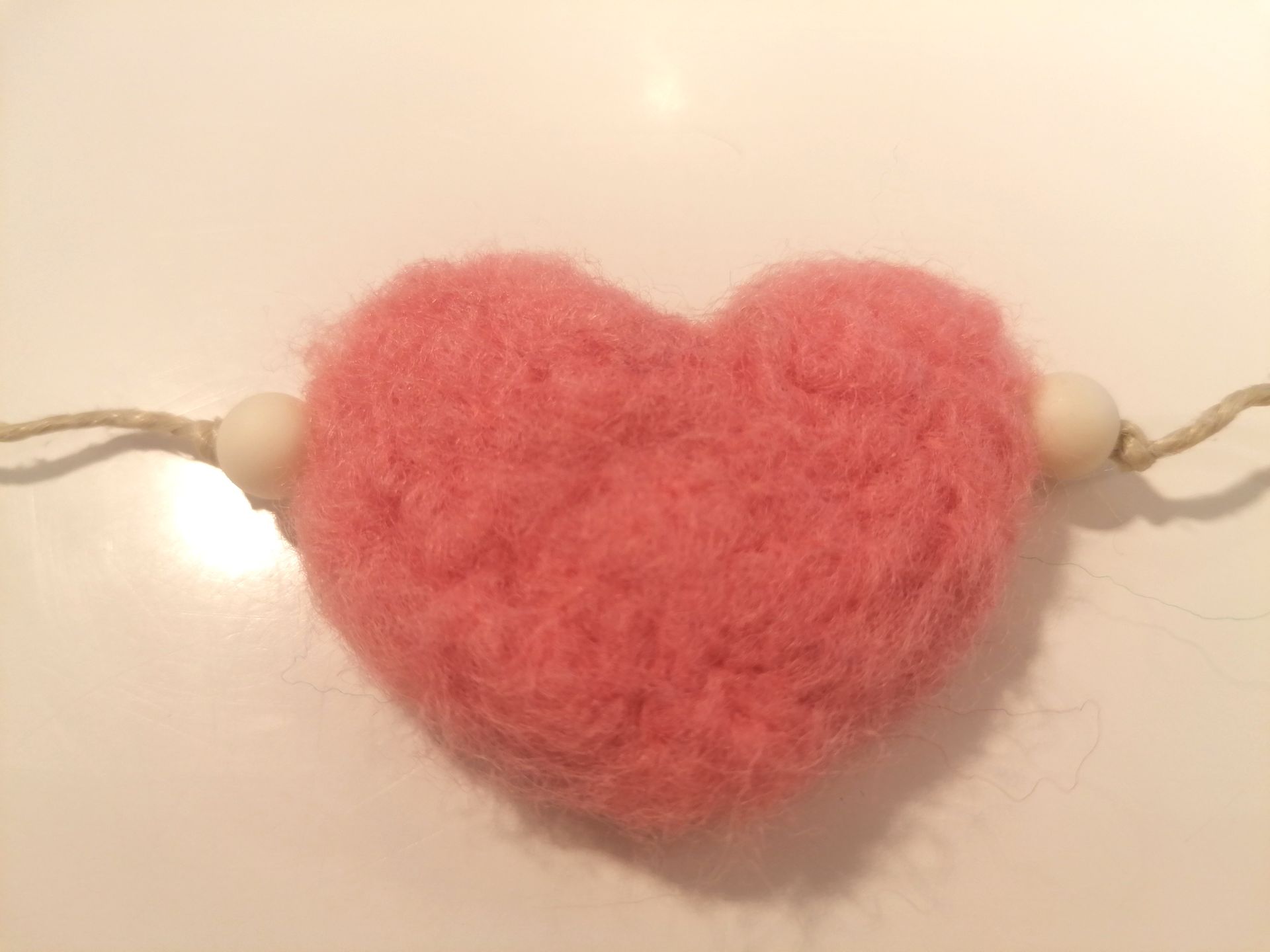 Roze, zacht hartje met twee witte kralen eraan vastgemaakt met een touwtje.