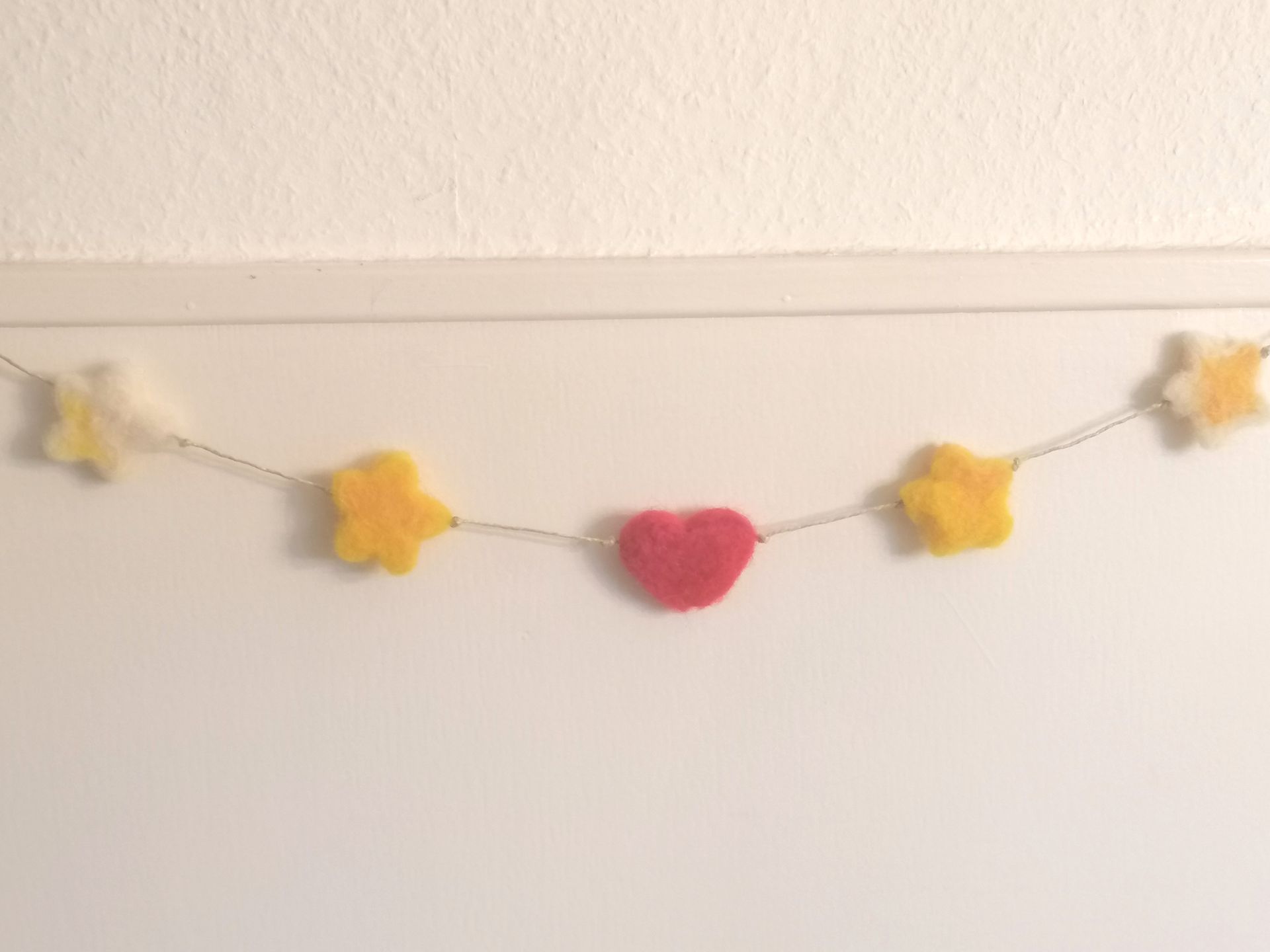 Vijf gevilte hartvormige ornamenten: rood, kastanjebruin en geel, geregen met kralen en touw.