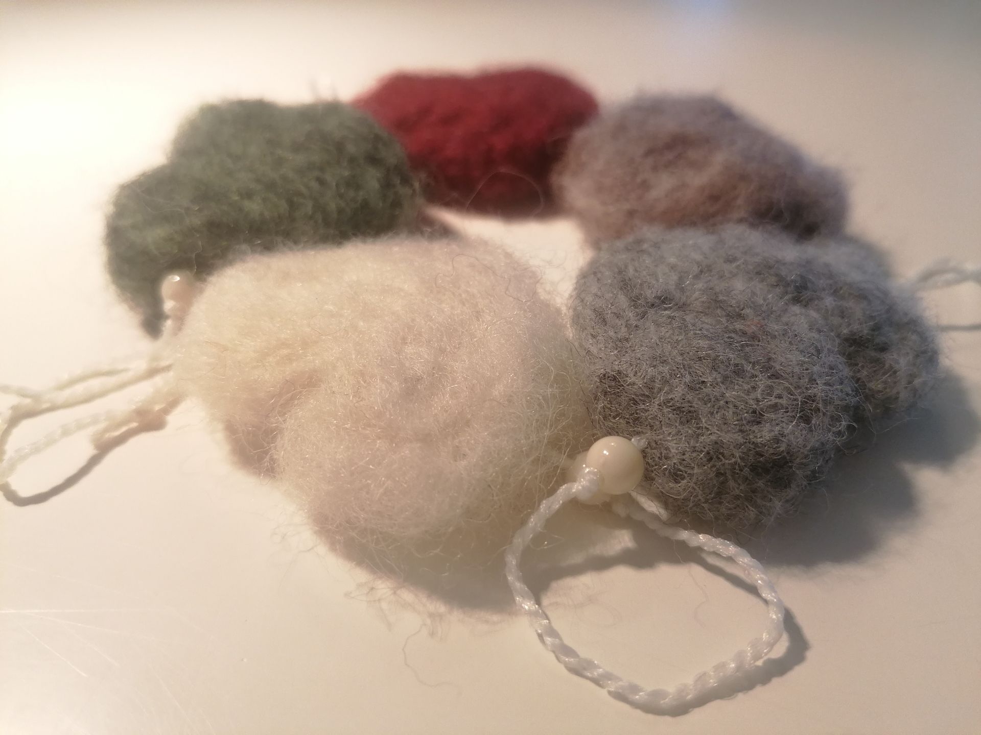 Zes zachte, wollige bollen in neutrale kleuren, elk met een touwtje eraan.