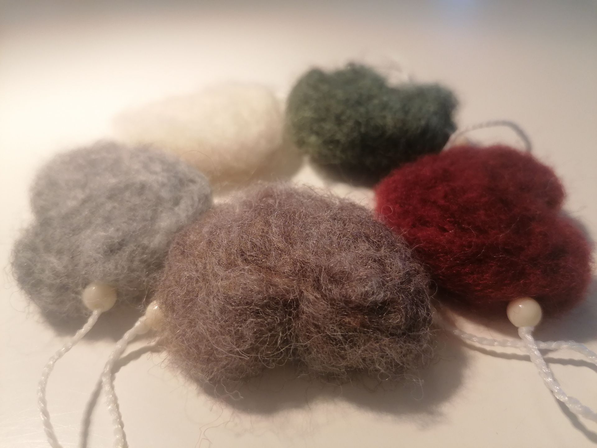Zes gevilte wollen hartvormige ornamenten in grijs, wit, groen, bruin en bordeauxrood, met wit touw en parelkralen.