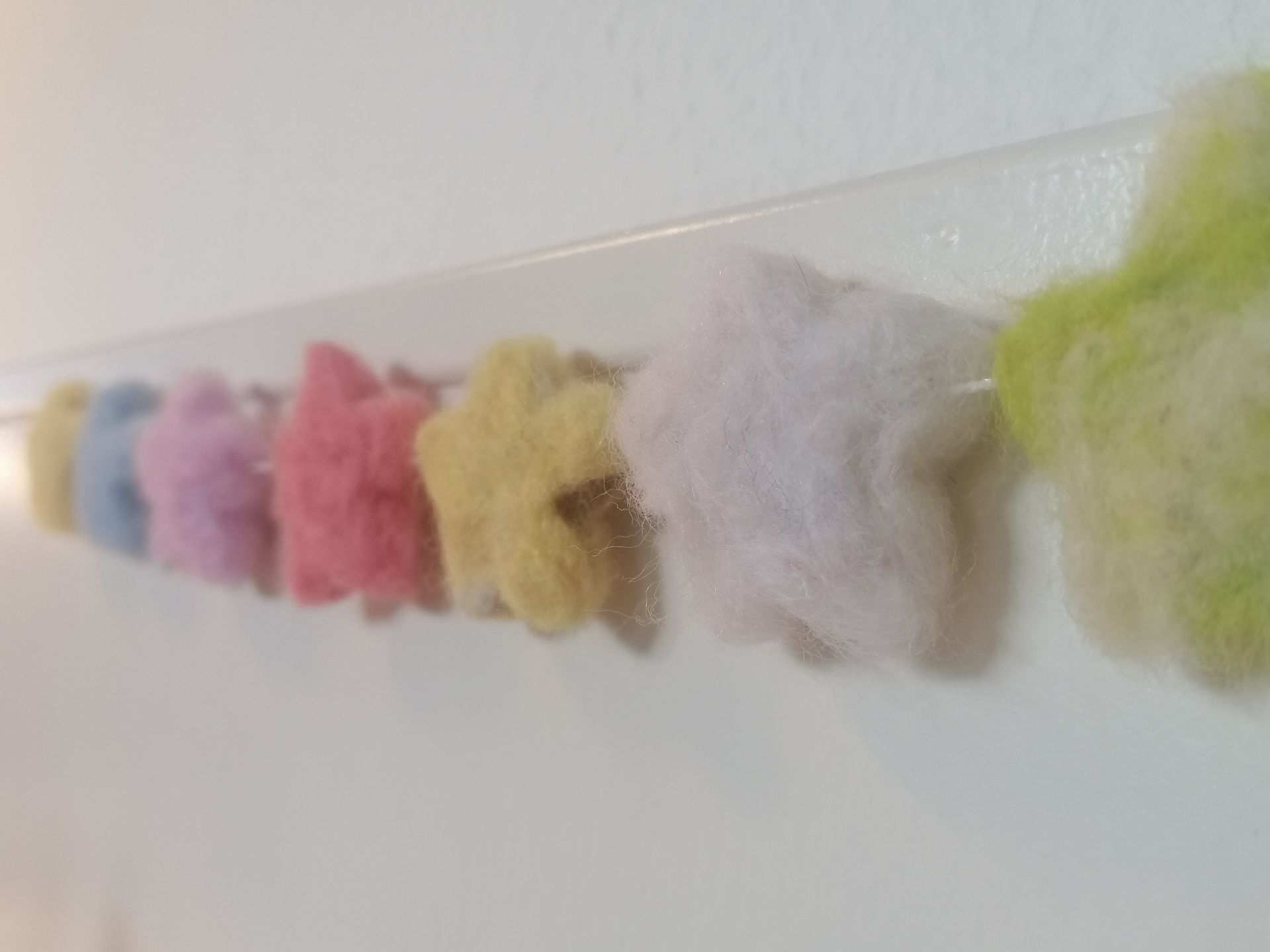 Zes zachte, wollige bollen in neutrale kleuren, elk met een touwtje eraan.