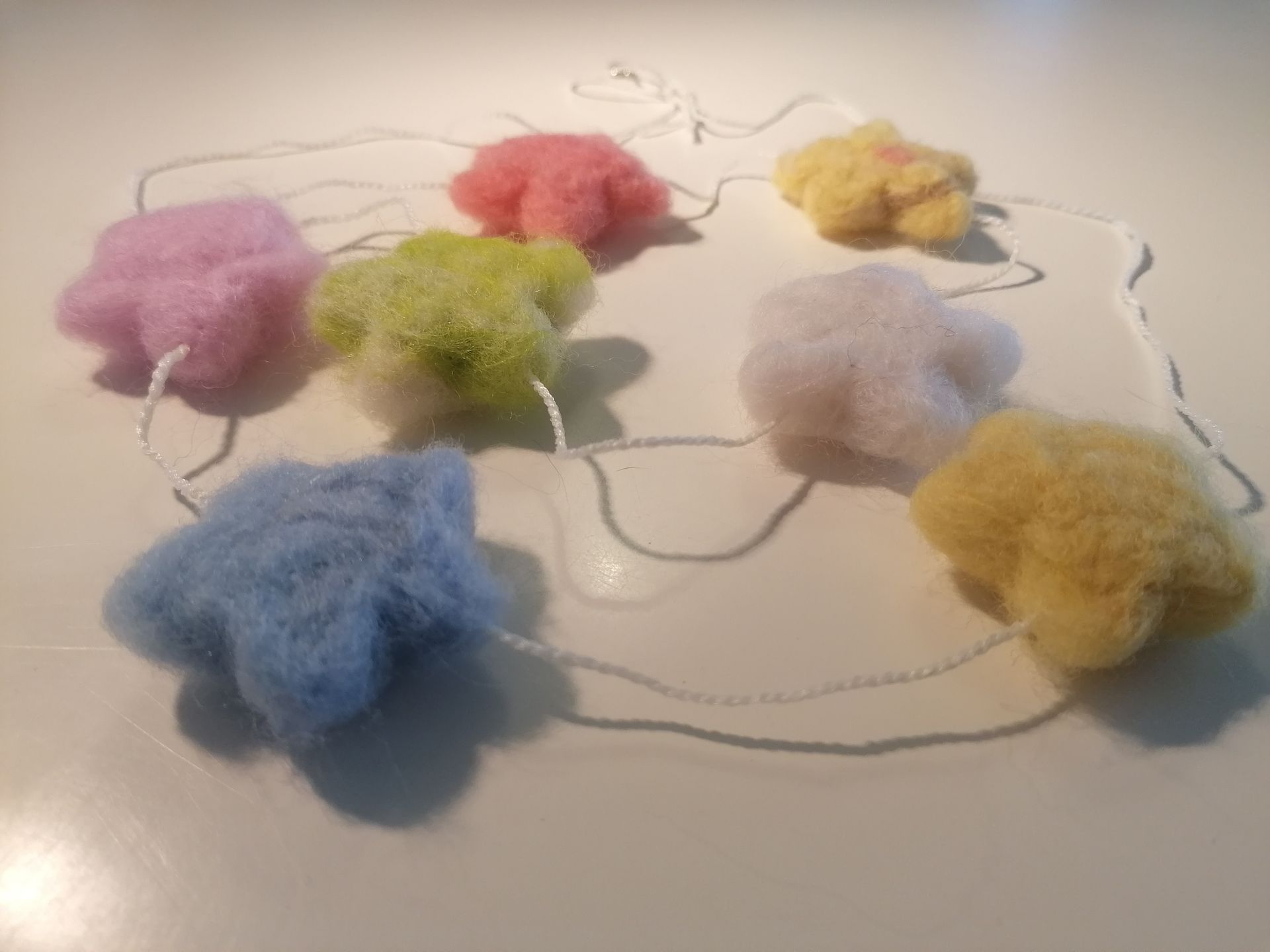 Zes gevilte wollen hartvormige ornamenten in grijs, wit, groen, bruin en bordeauxrood, met wit touw en parelkralen.