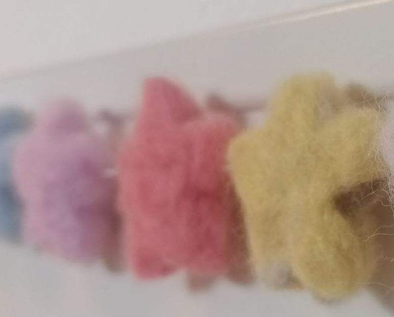 Groen, hartvormig, wol object met een witte kraal eraan.