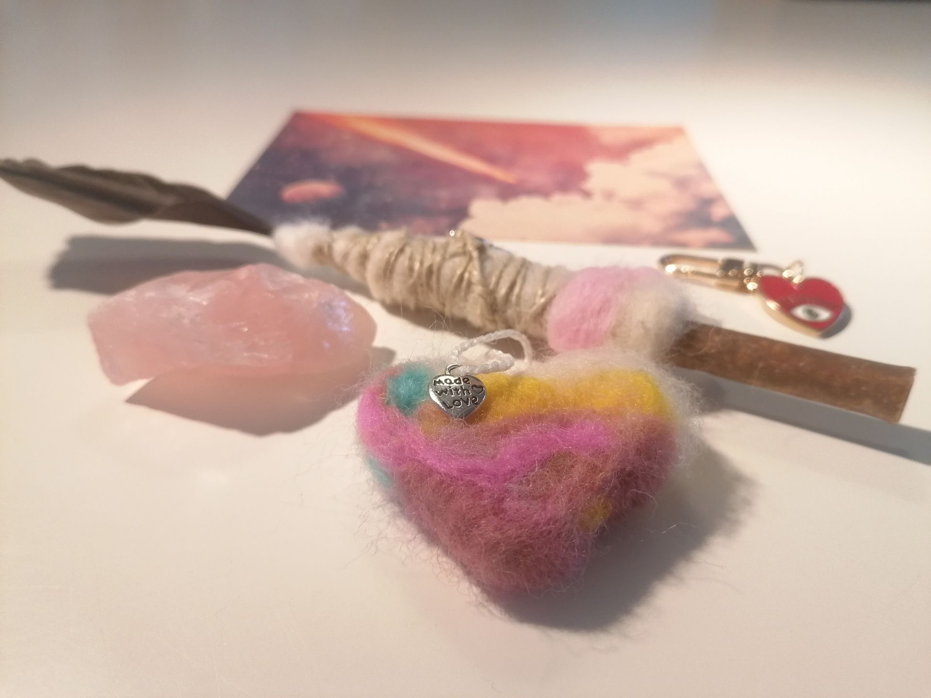 Rozenkwartskristal met een smudgeveer, wollen hartje en decoratieve sleutelhanger.