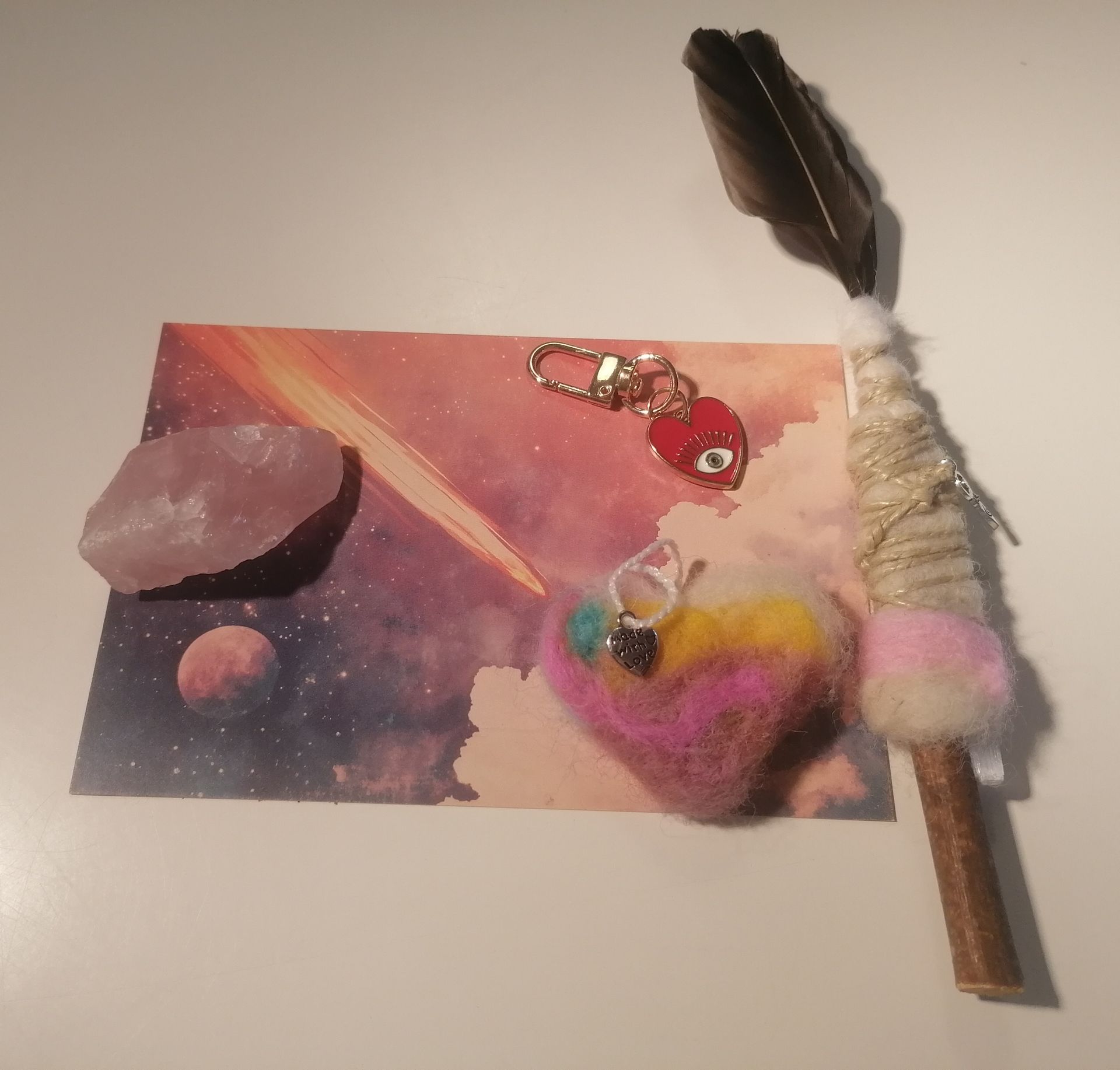 Rozenkwartskristal met een smudgeveer, wollen hartje en decoratieve sleutelhanger.