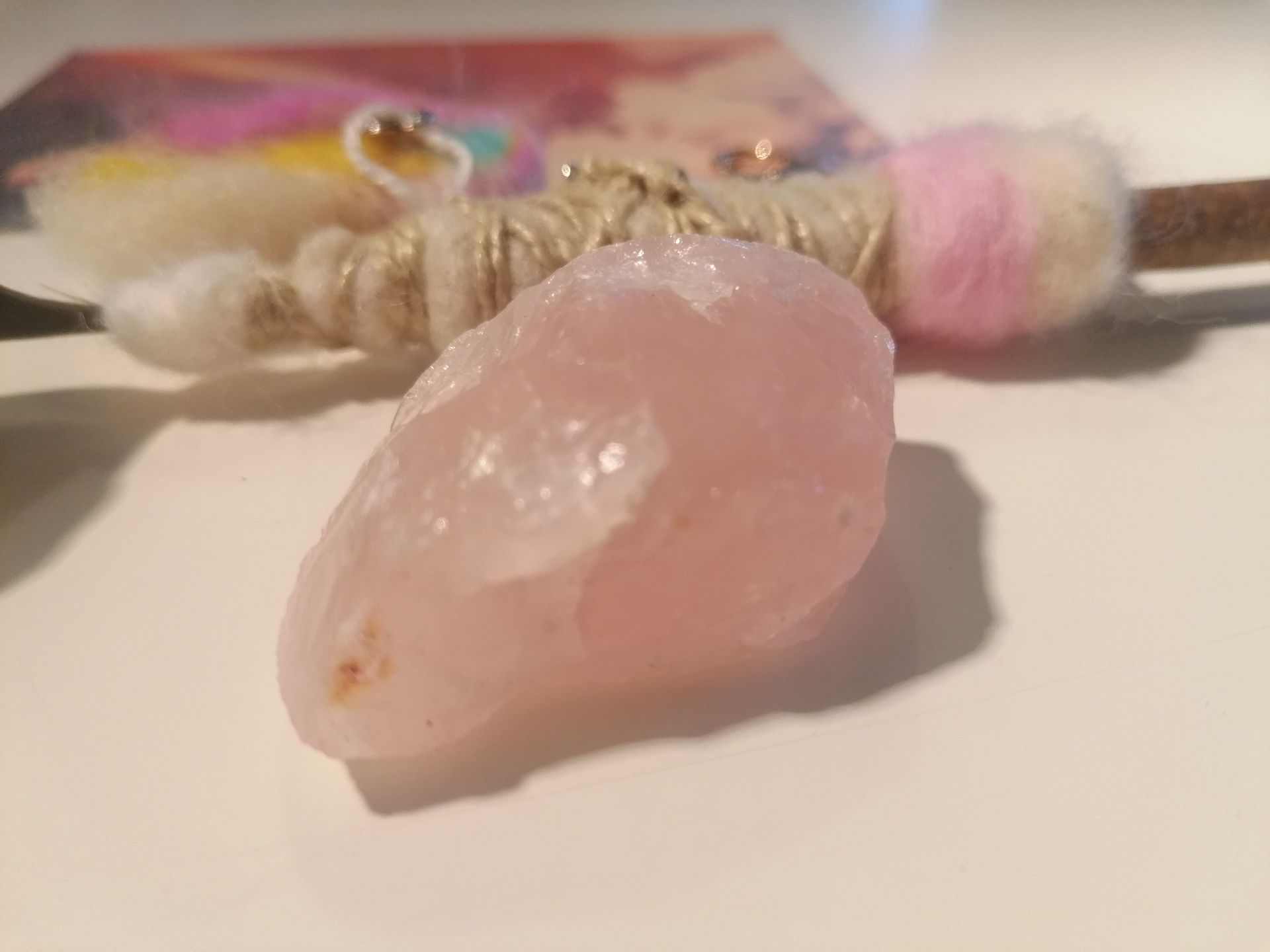 Rozenkwartskristal met een smudgeveer, wollen hartje en decoratieve sleutelhanger.