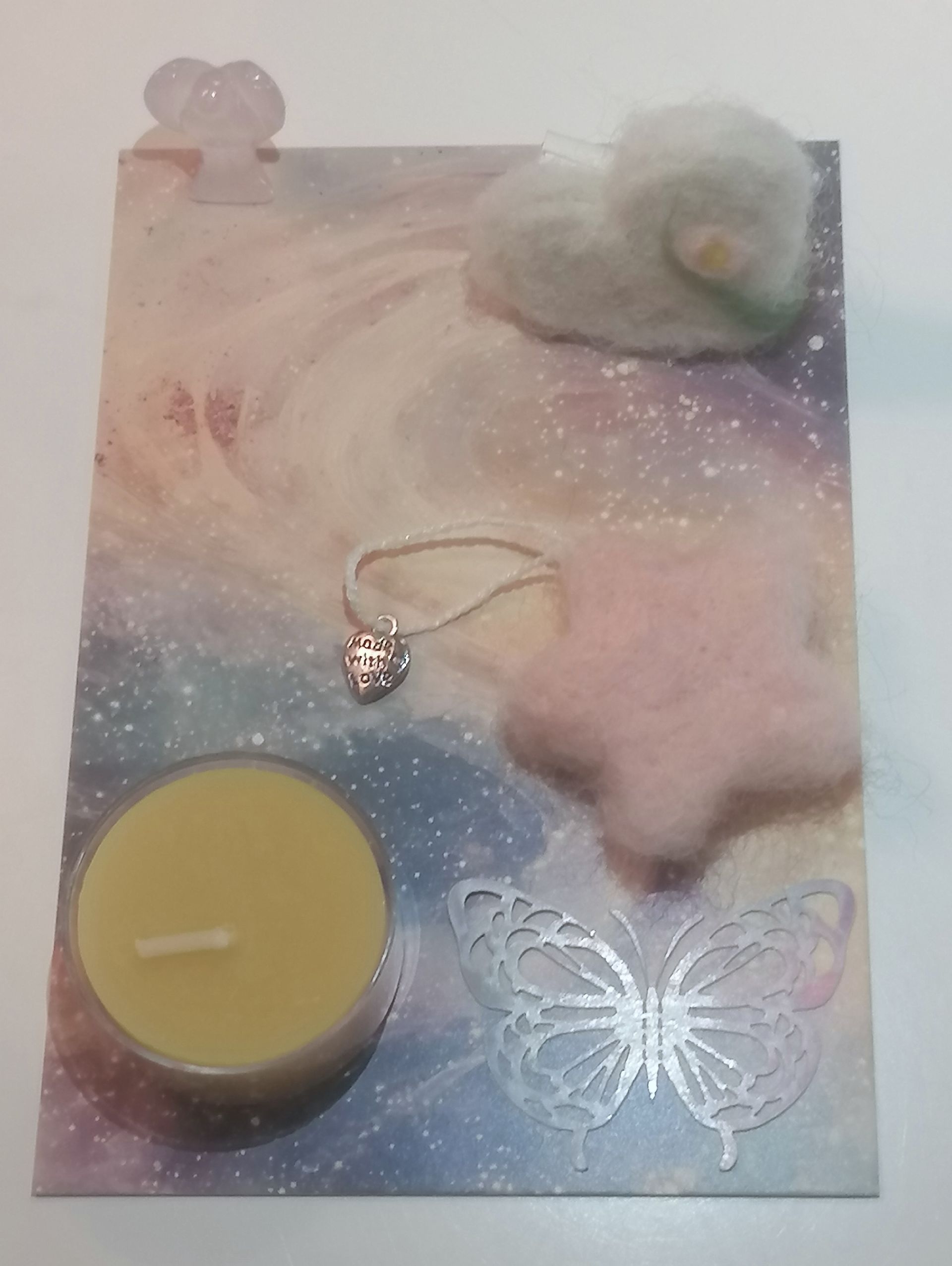 Een decoratieve kaart met een waxinelichtje, wol ornament in de vorm van hart met boodschap,een ster van wol en een vlinder.