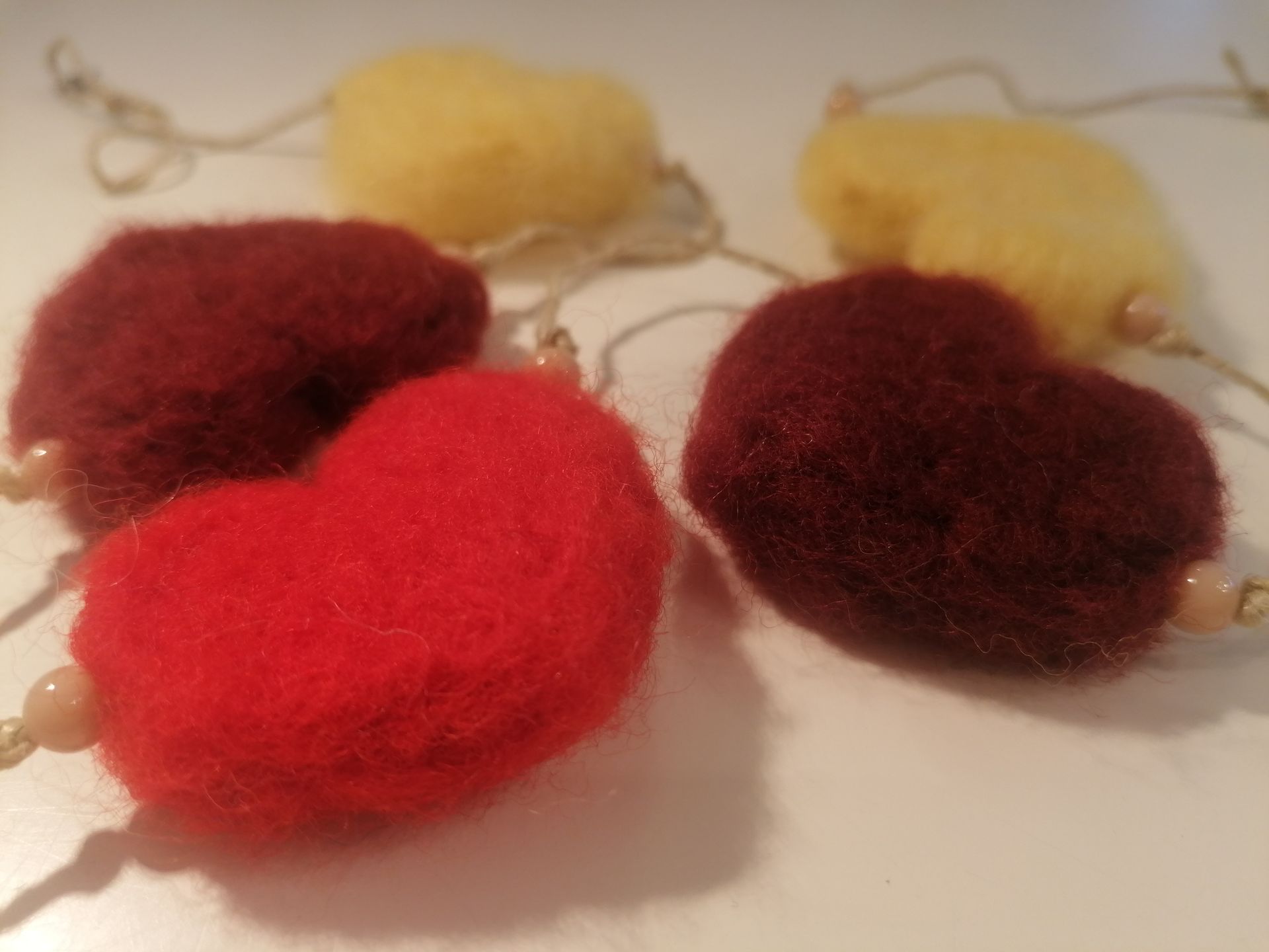 Vijf gevilte hartvormige ornamenten: rood, kastanjebruin en geel, geregen met kralen en touw.