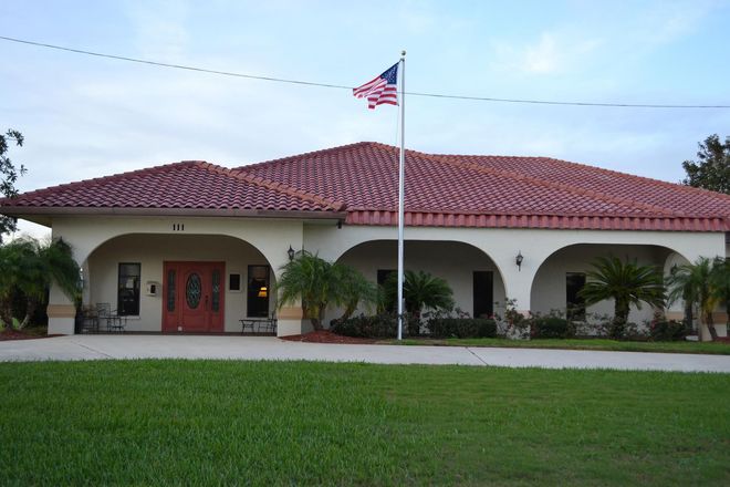 A building with a red tile roof, American flag, and green lawn in front.