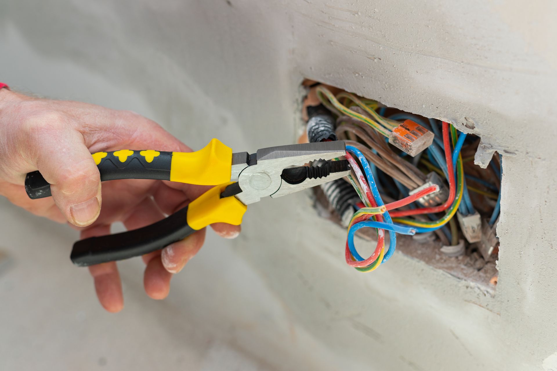 Hand Holding Pliers Cutting Exposed Coloured Electrical Wires — Local Light Electrical in Brunswick Heads, NSW