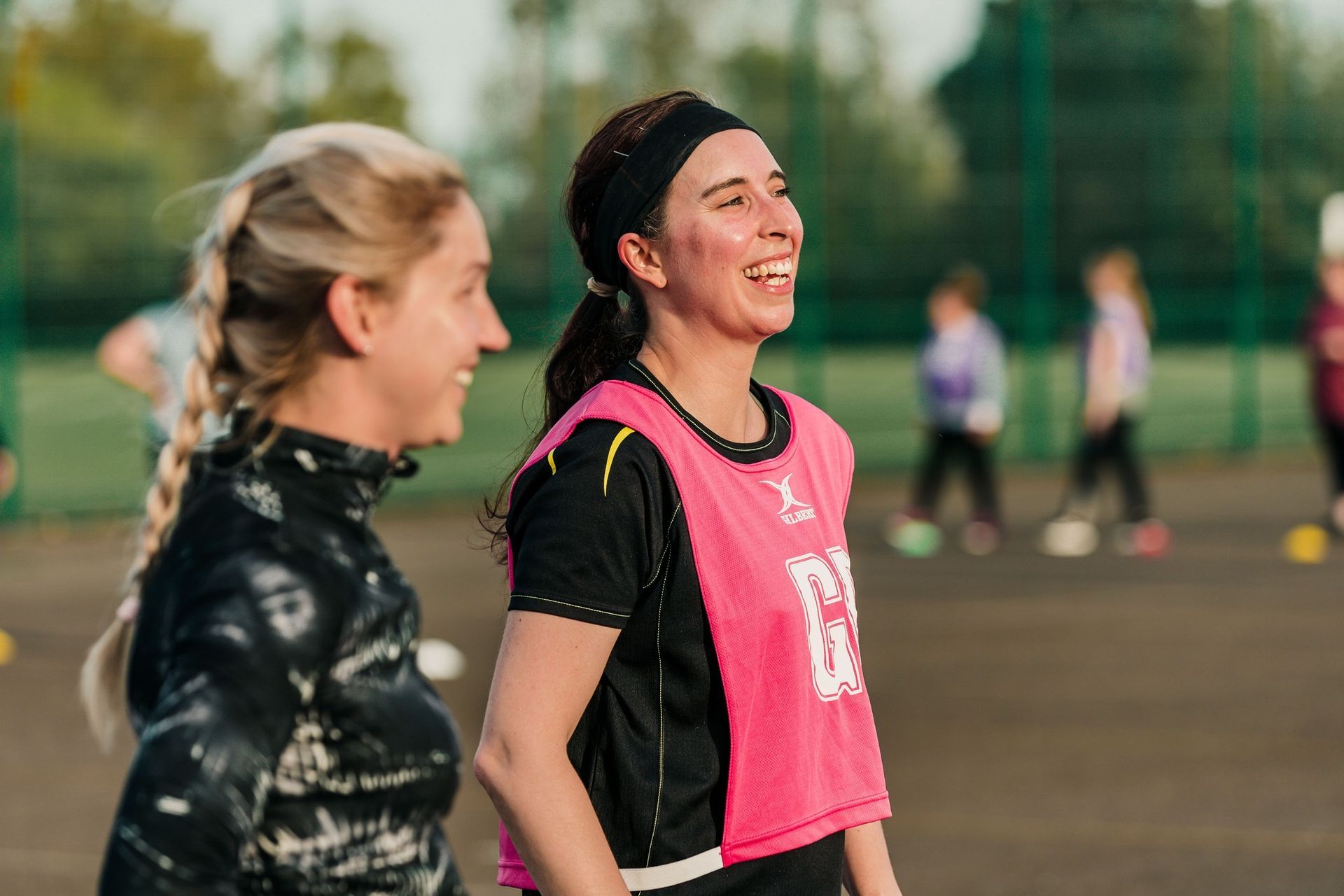 Two women are standing next to each other on a soccer field and smiling.