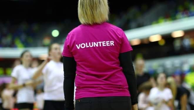 A woman wearing a pink volunteer shirt is standing in front of a crowd.