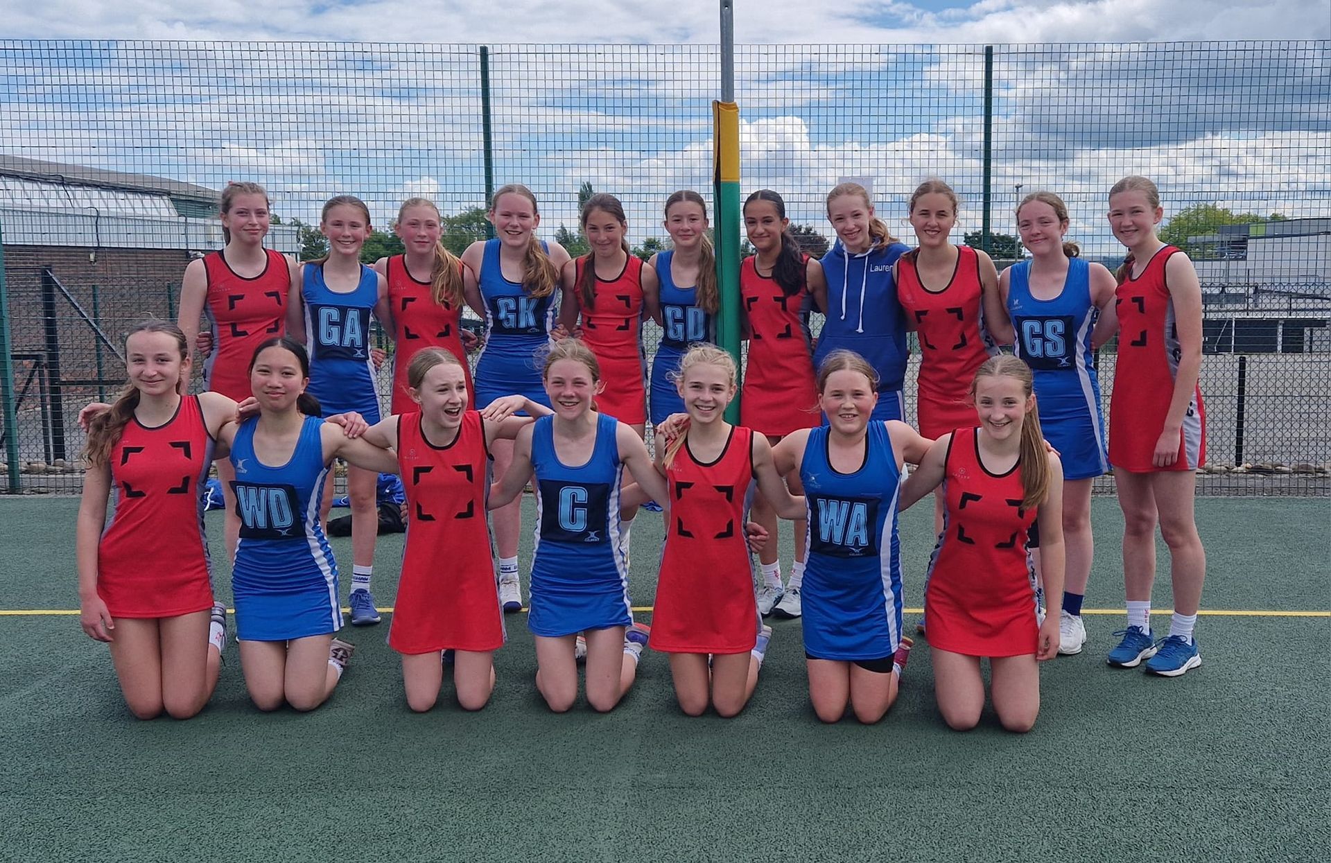 A group of young girls are posing for a picture on a netball court.