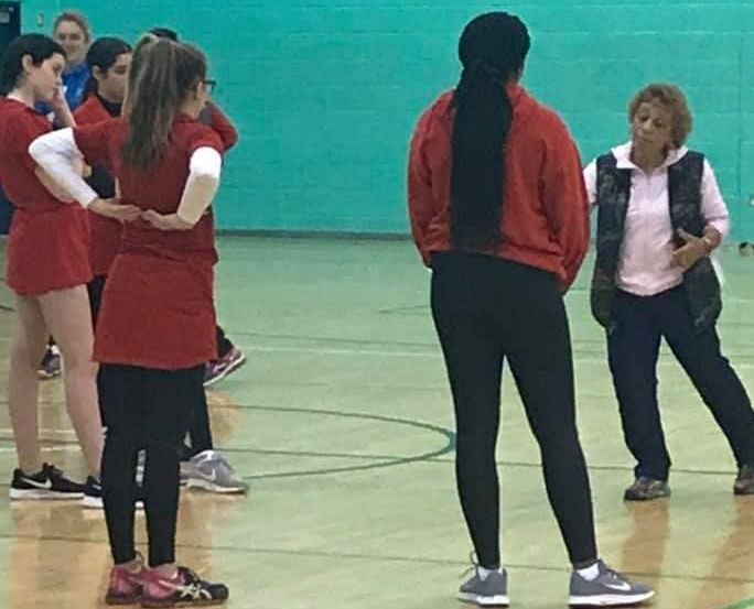 A group of women are standing on a basketball court talking to each other.