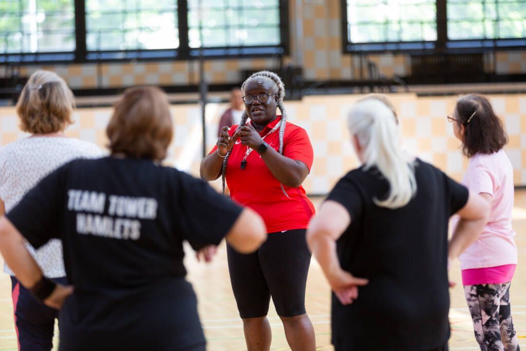 A woman in a red shirt is talking to a group of women in black shirts.