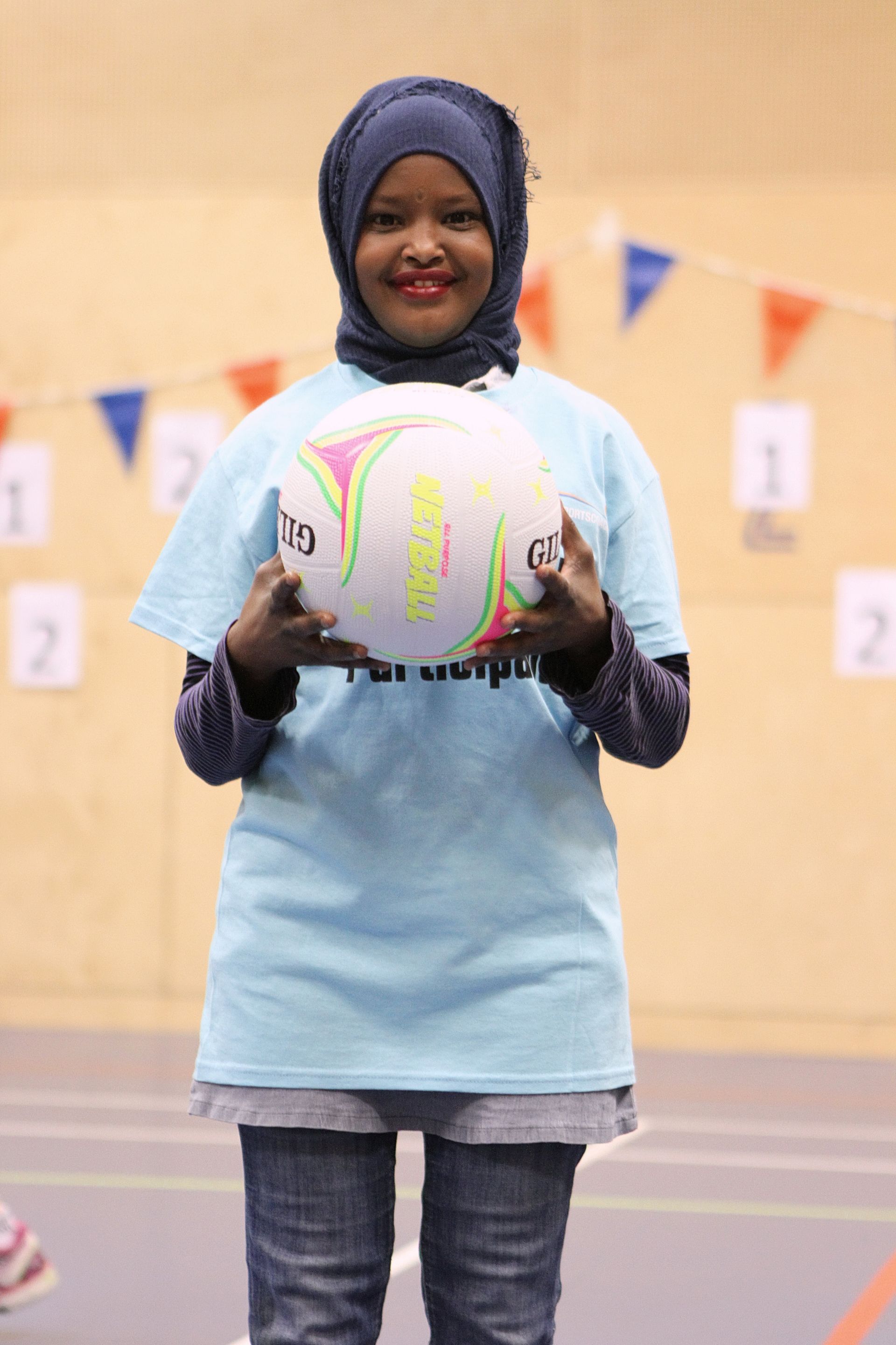 A woman wearing a hijab is holding a volleyball in her hands
