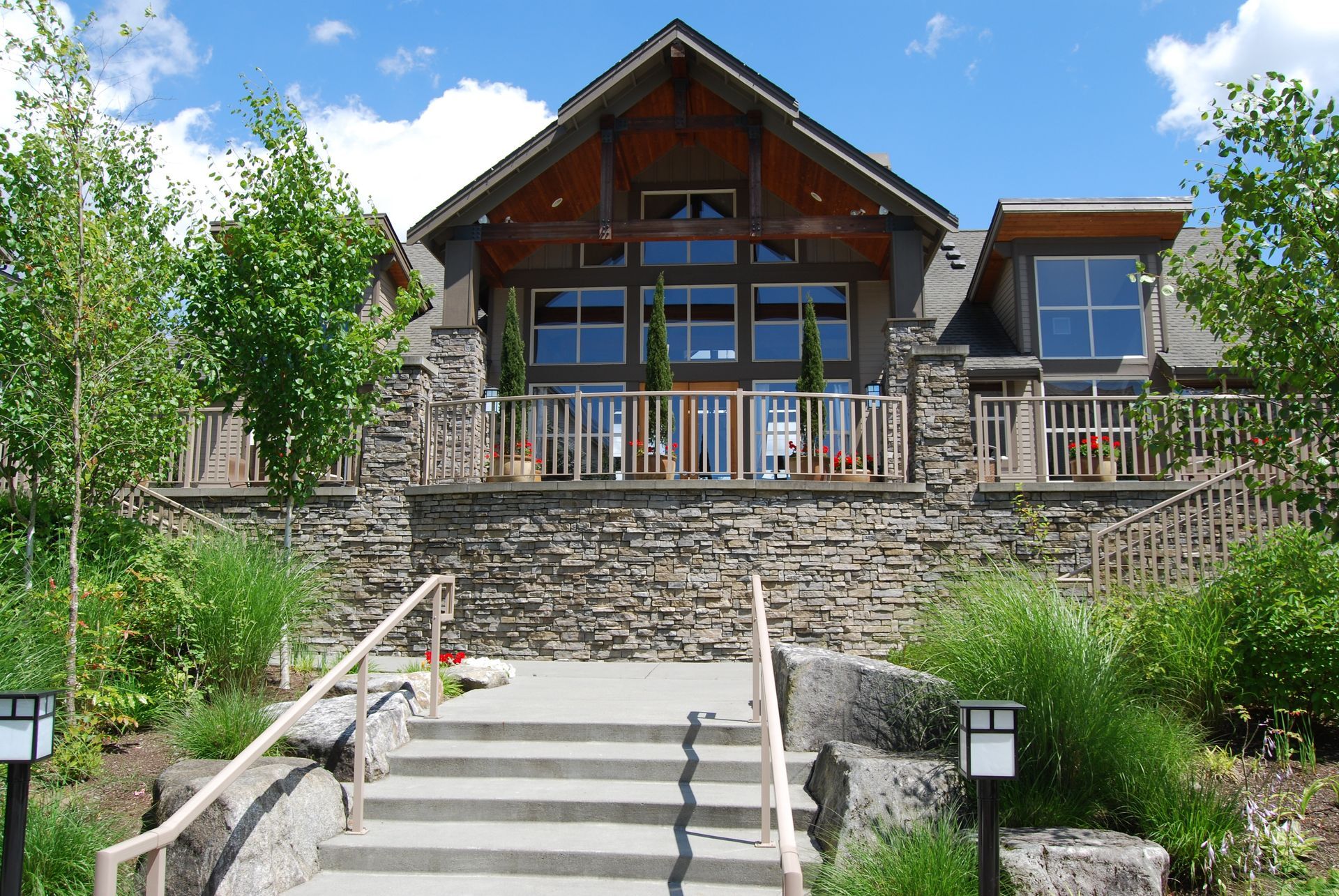 Stone house with a wooden balcony, front steps, and landscaped garden under a blue sky