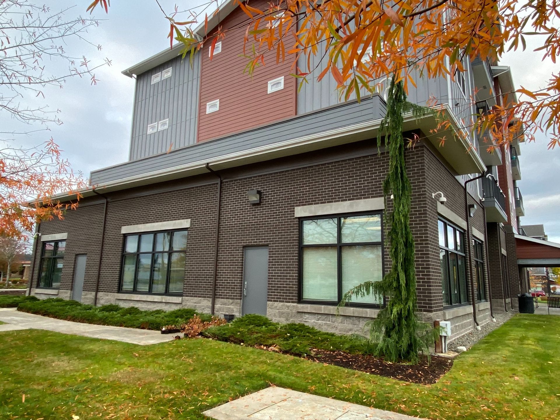 Modern two-story building with stone and wood siding, large windows, and a grassy lawn in autumn.