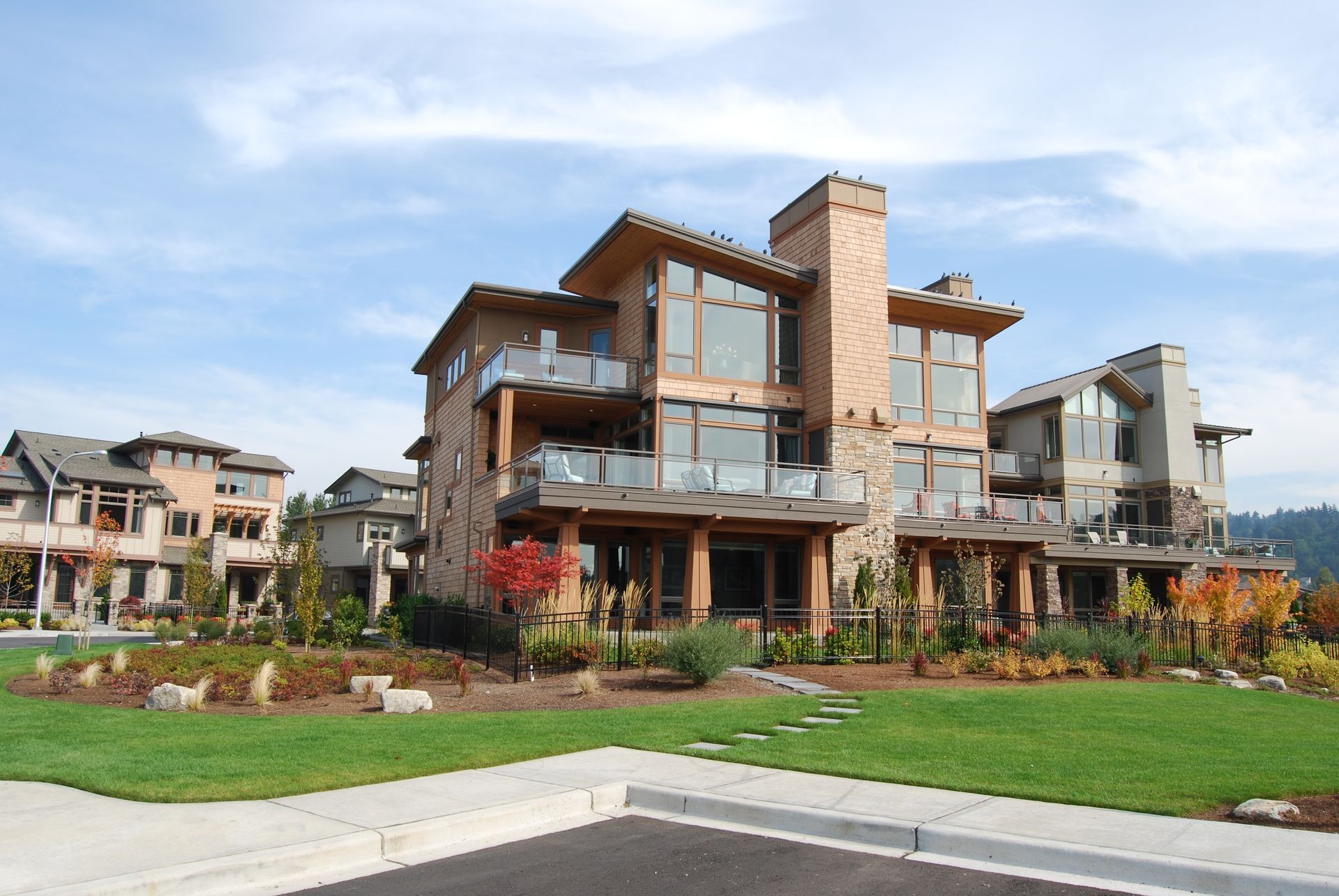 Modern multi-story townhouse with wood and stone exterior, landscaped lawn, and blue sky