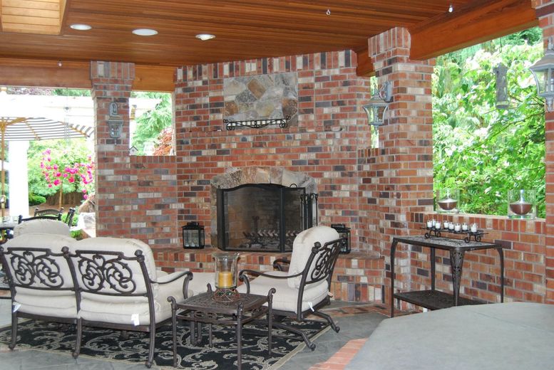 Brick patio with covered fireplace, wrought-iron seating, and views of a lush garden