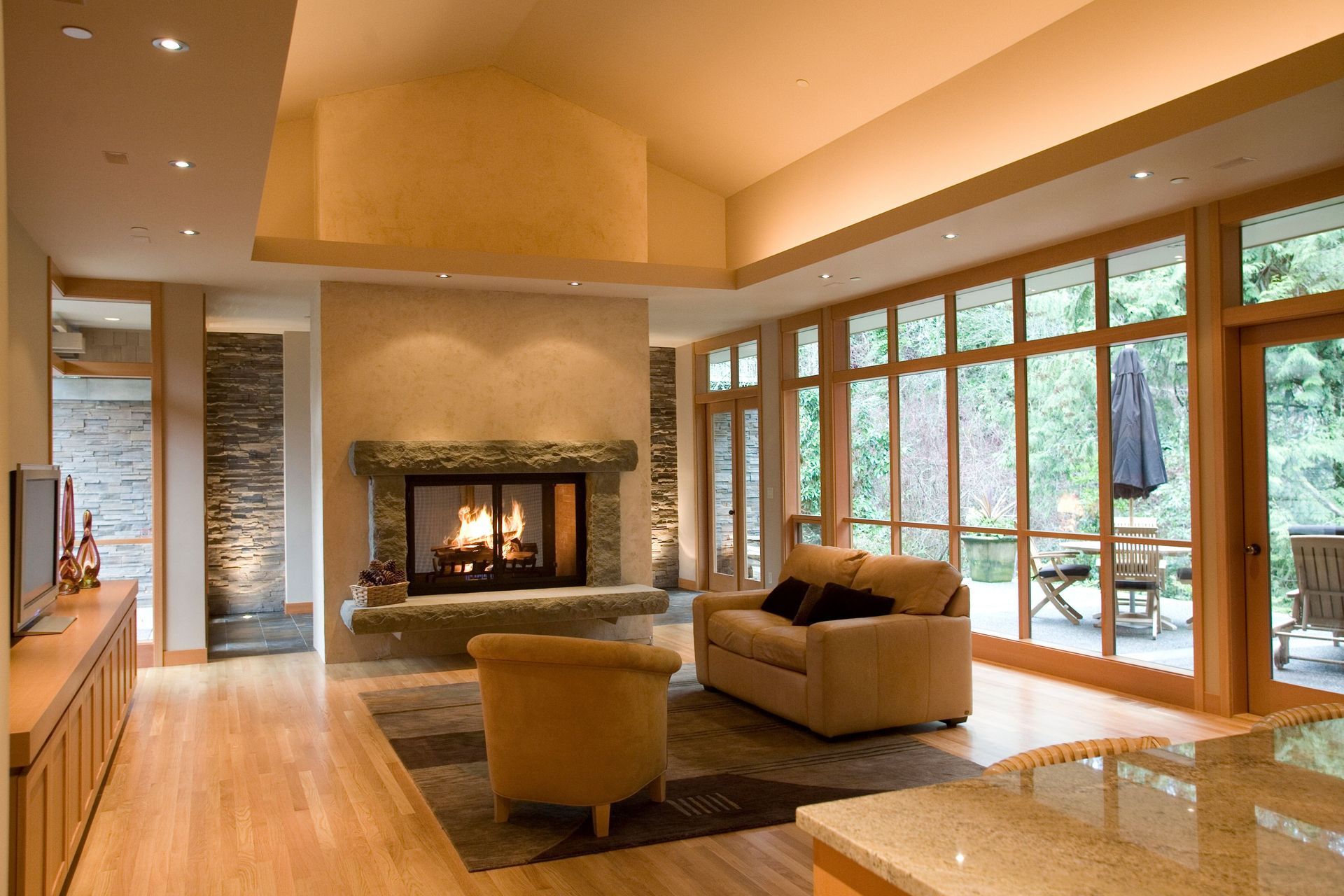 Modern living room with a fireplace, beige seating, and large windows overlooking trees