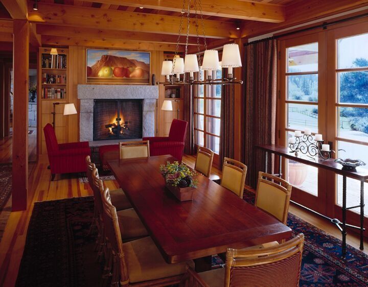 Cozy wood-paneled dining room with long table, red chairs, fireplace, and large windows overlooking snow.