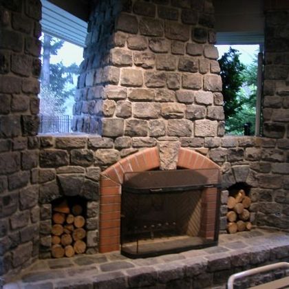 Stone fireplace with brick arch and stacked firewood in a rustic room
