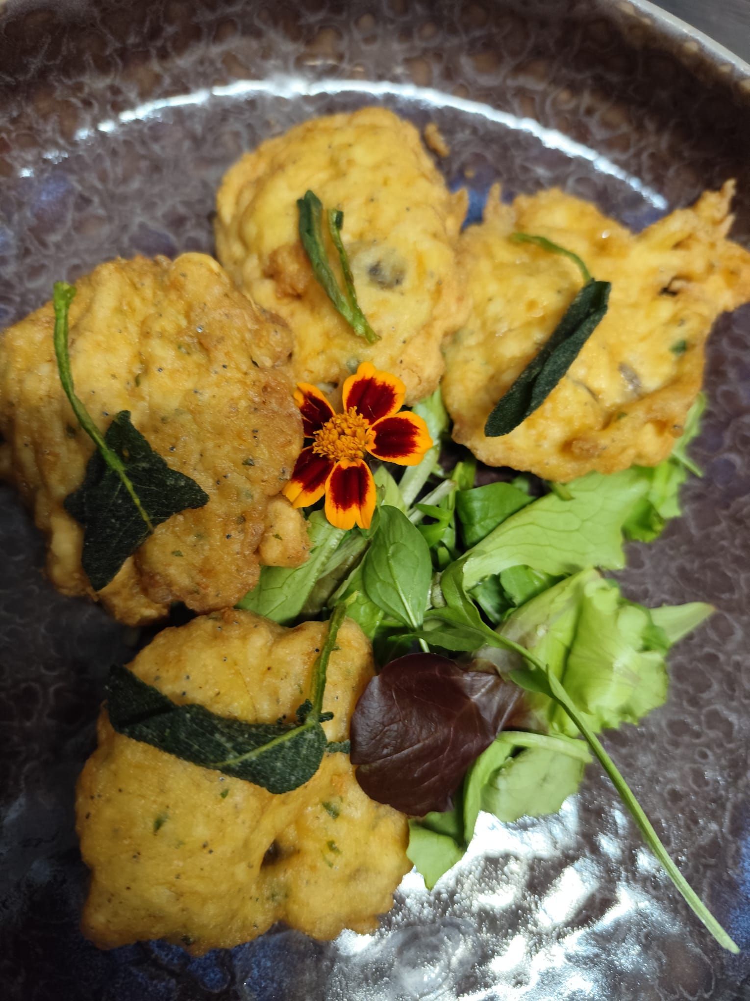 Cibo fritto su verdure, guarnito con fiori ed erbe commestibili, servito su un piatto marrone.