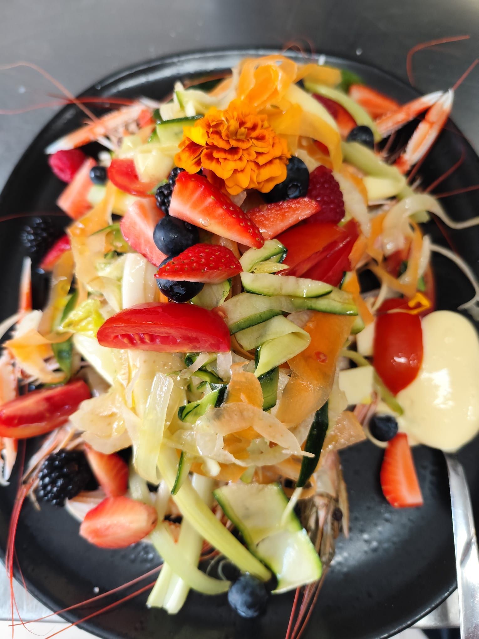 Insalata di mare colorata con bacche, verdure e fiori commestibili su un piatto nero.