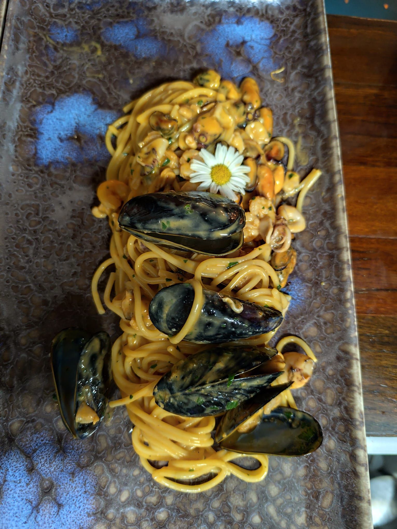 Spaghetti alle cozze, guarniti con fiori, su un piatto decorato blu-marrone.