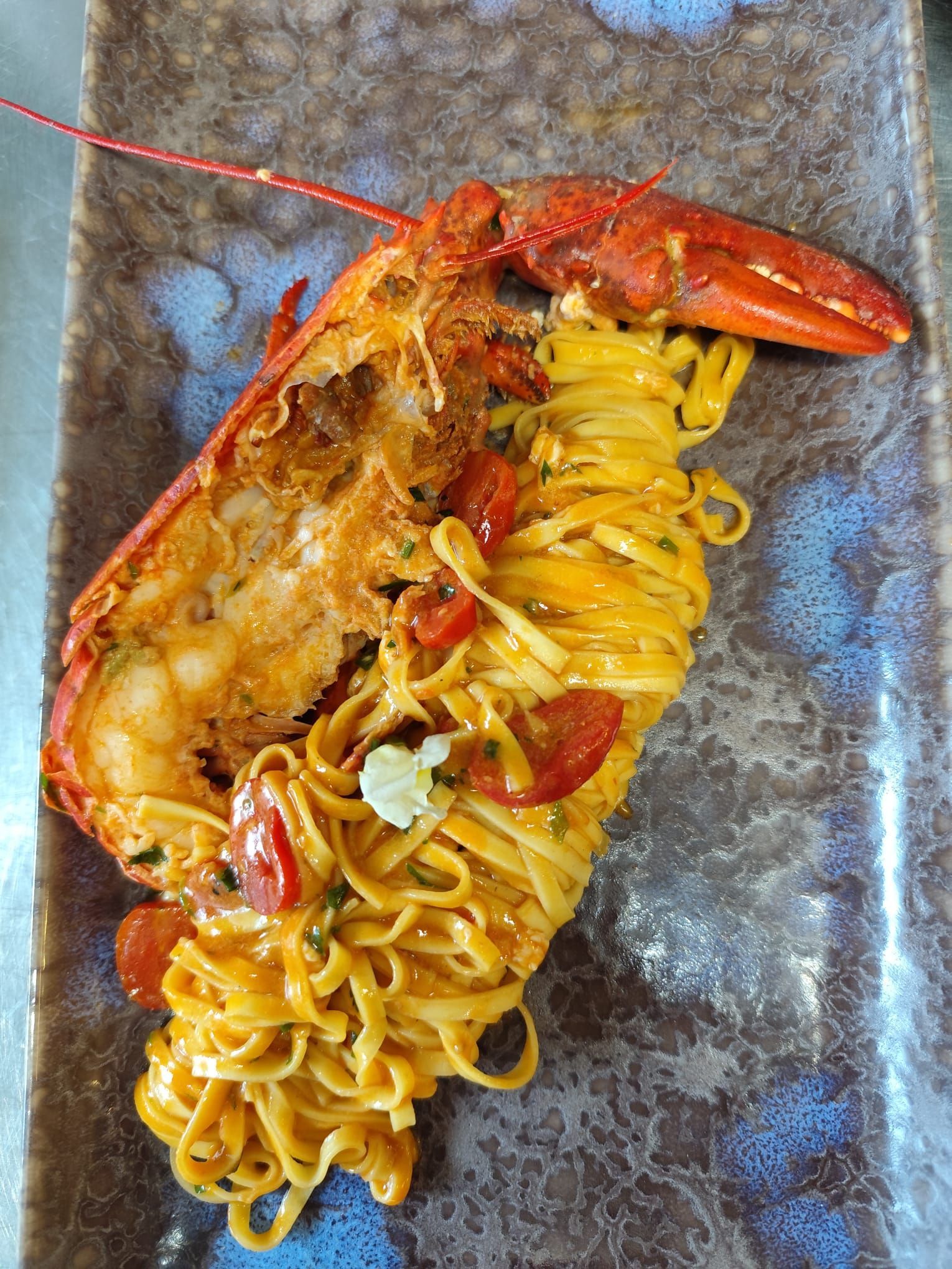 Piatto di pasta e aragosta, aragosta rossa, pasta gialla, pomodorini, su un piatto decorato con motivi blu.