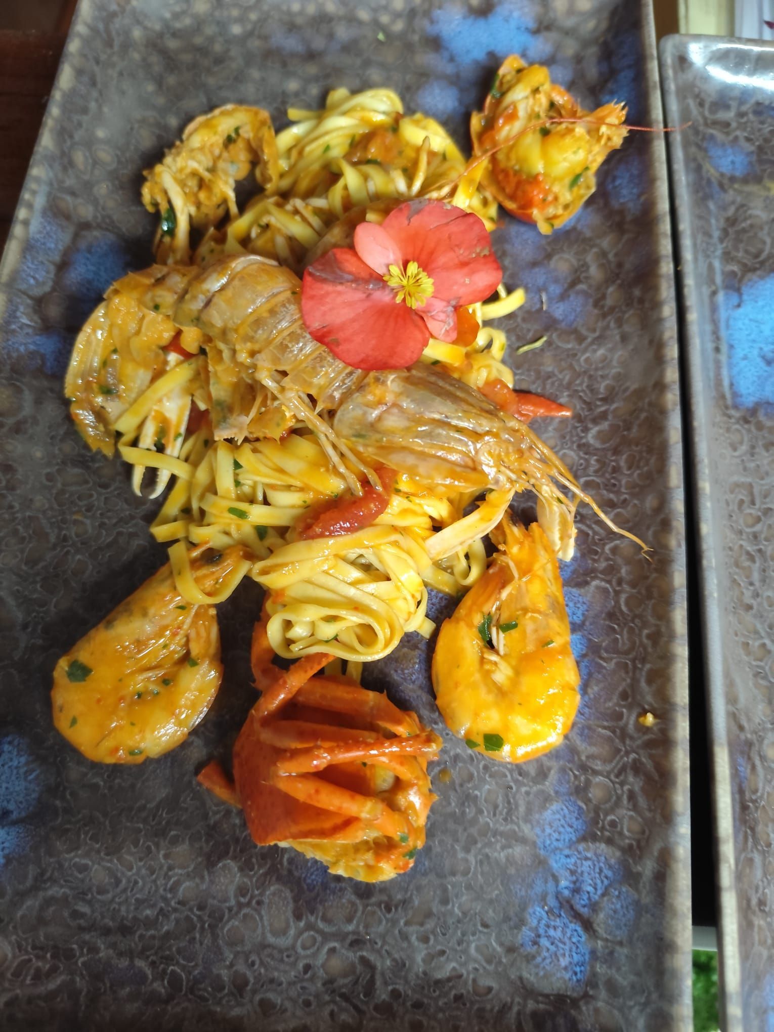 Piatto di pasta con gamberi e guarnizione floreale su un piatto rettangolare.