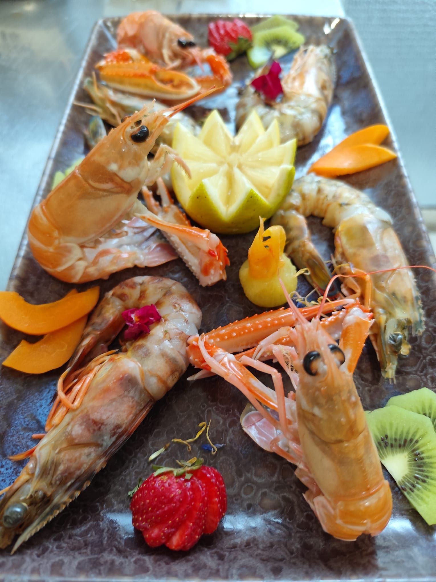 Piatto di gamberi cotti con limone, frutta e guarnizione decorativa.