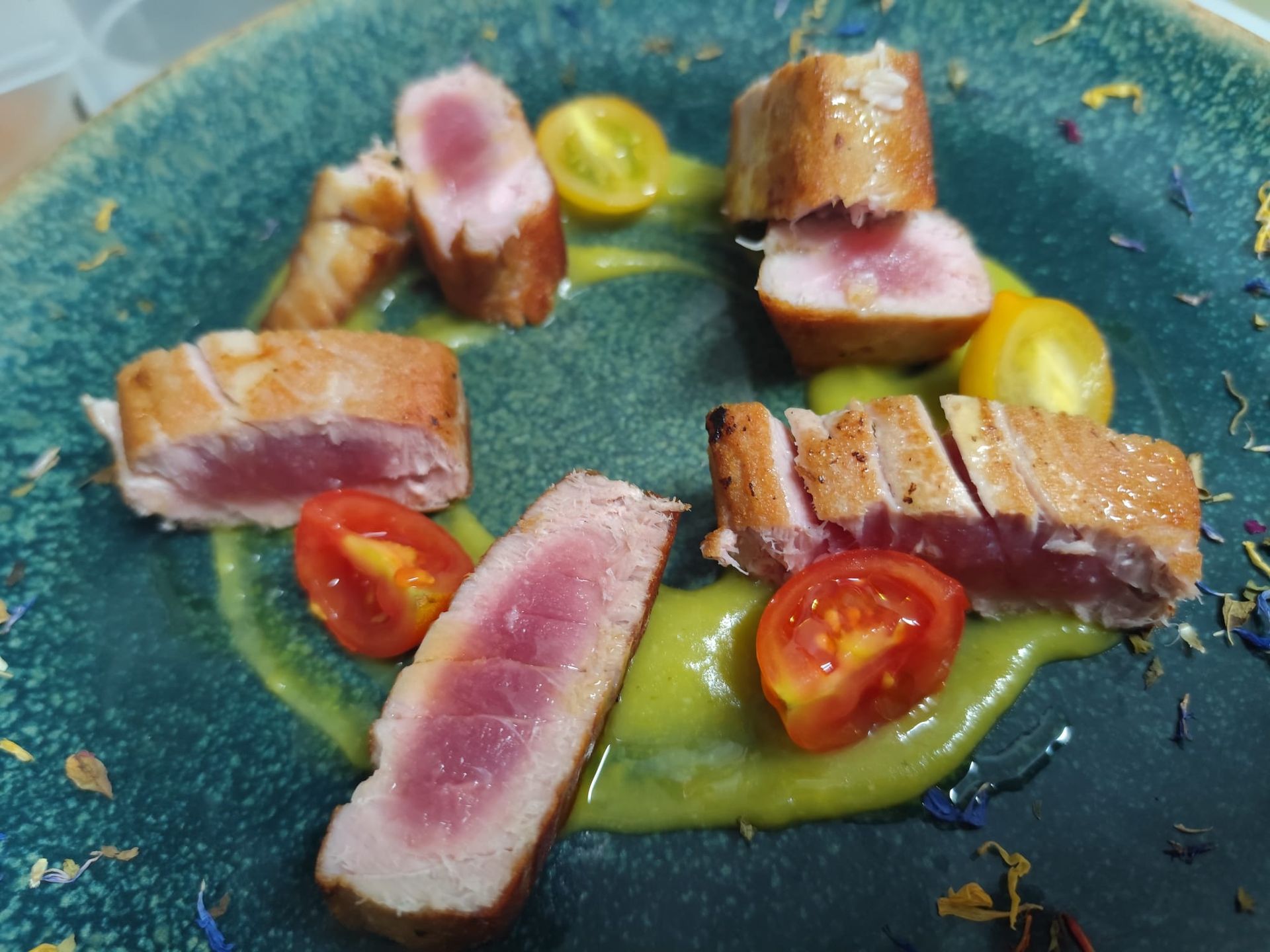 Fette di tonno scottato con cuore rosa su salsa verde, circondate da pomodori gialli e rossi tagliati a metà.