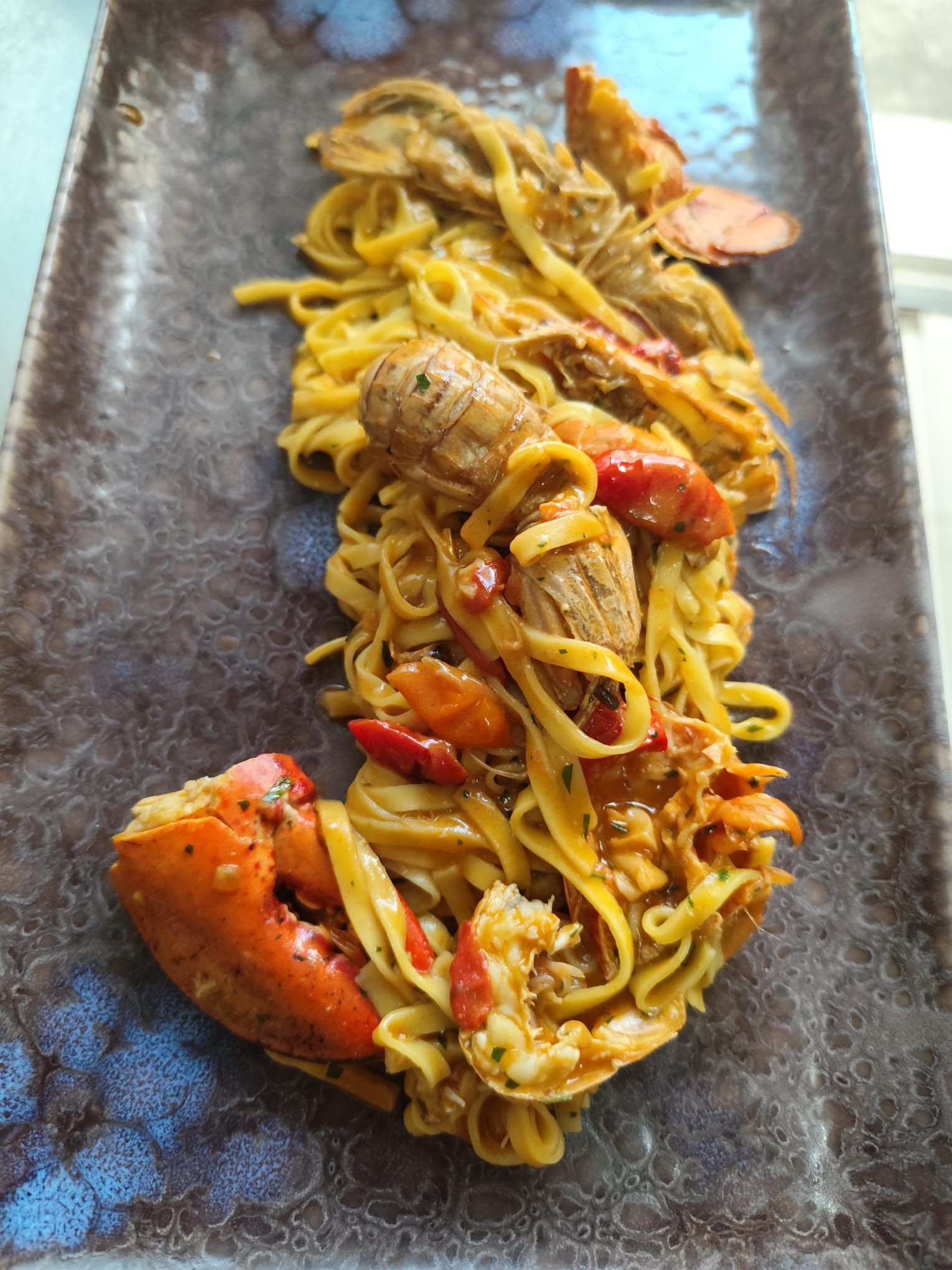 Pasta all'astice su un piatto rettangolare; astice arancione e tagliatelle gialle.