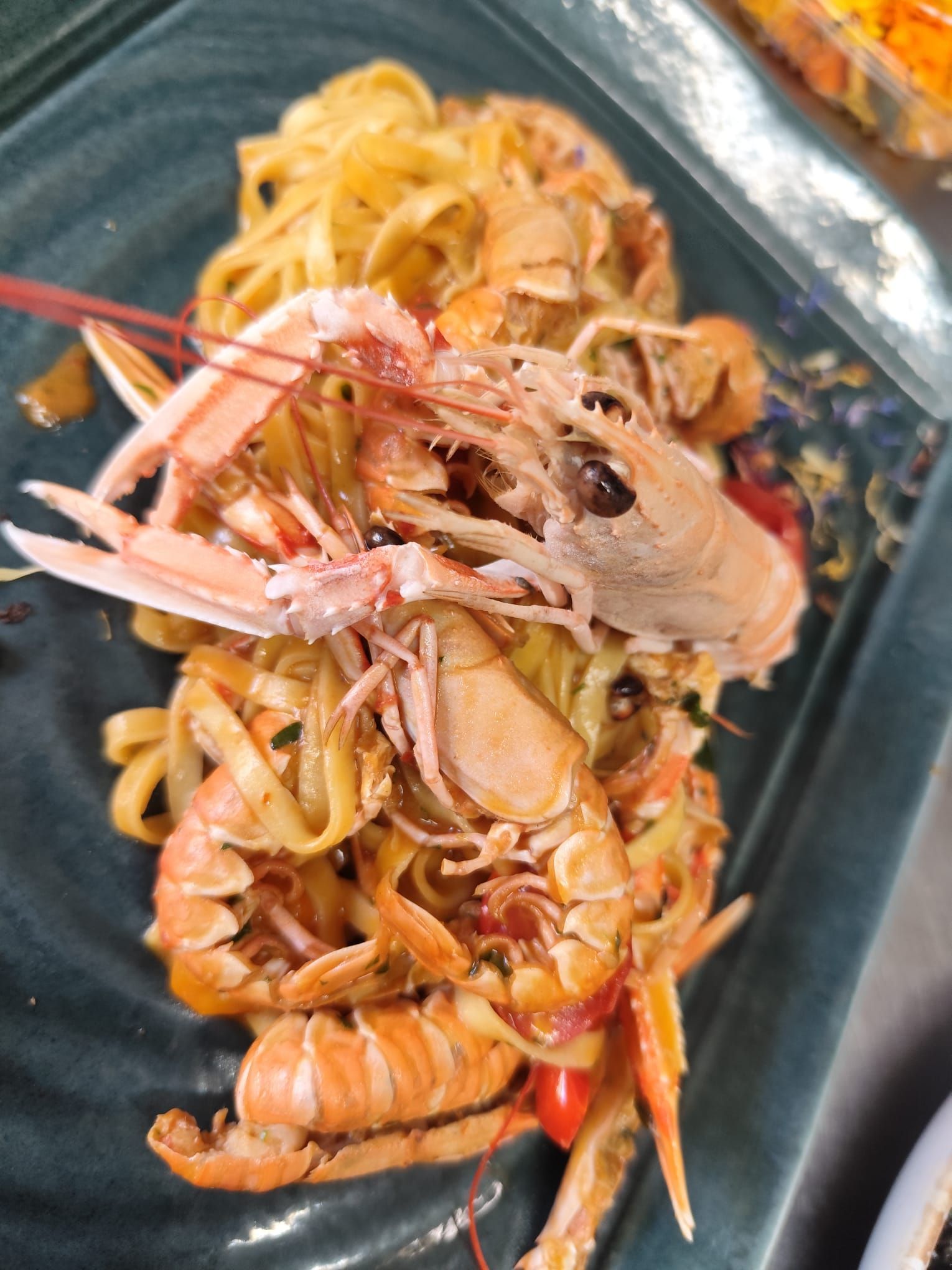 Piatto di pasta con frutti di mare cotti su un piatto rettangolare scuro.