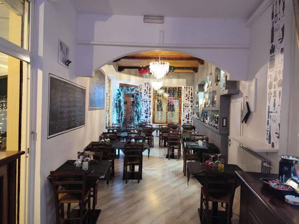 Interno di un ristorante con tavoli apparecchiati per cenare, bottiglie di vino sugli scaffali e una porta ad arco.