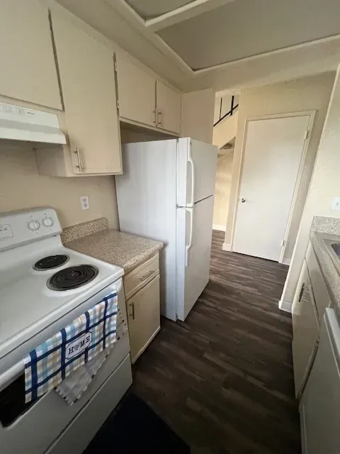 Kitchen with white appliances, cabinets, and dark wood-look flooring.