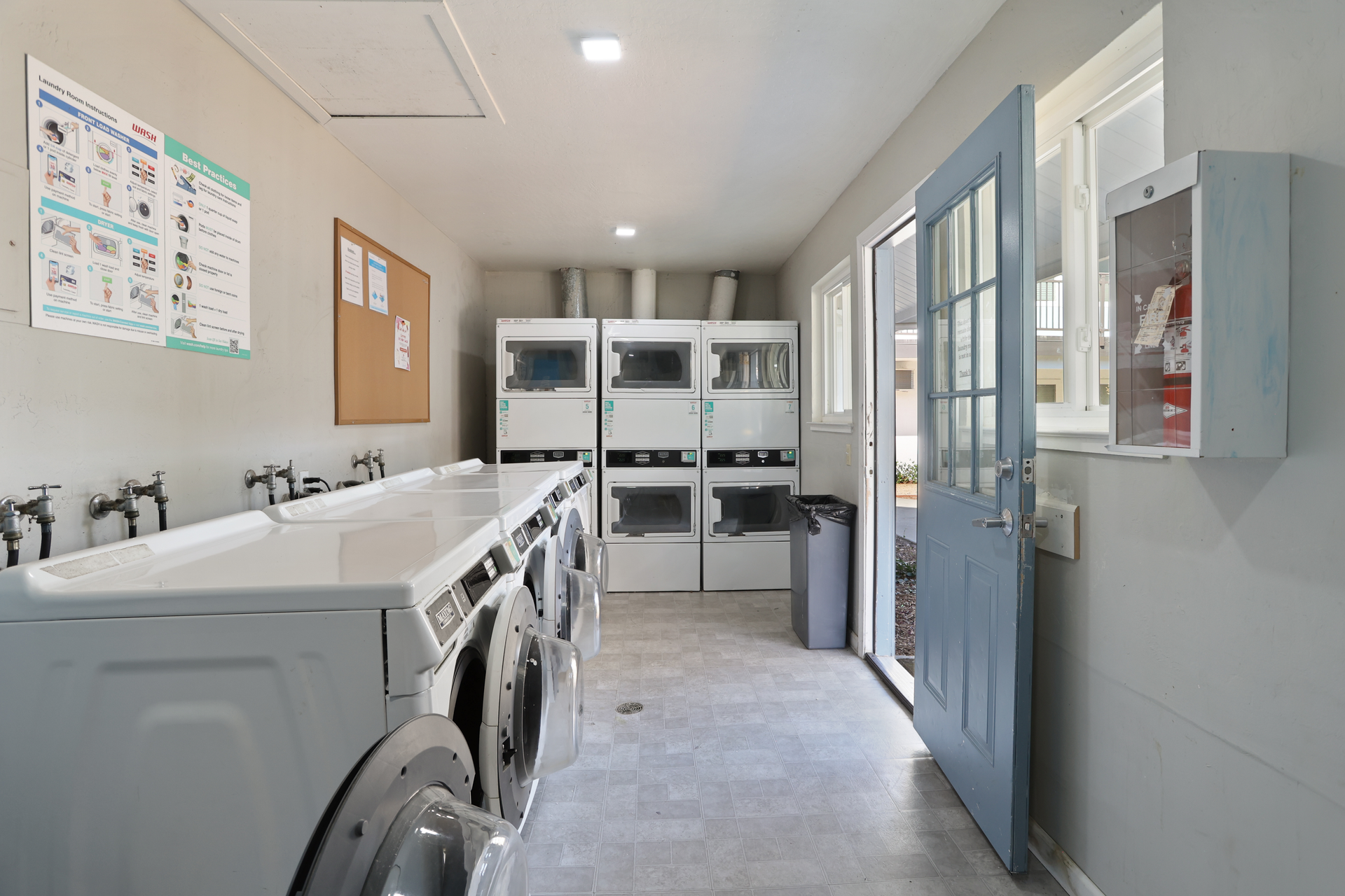 Laundry room with washers, dryers, storage shelves, and a blue door on the right