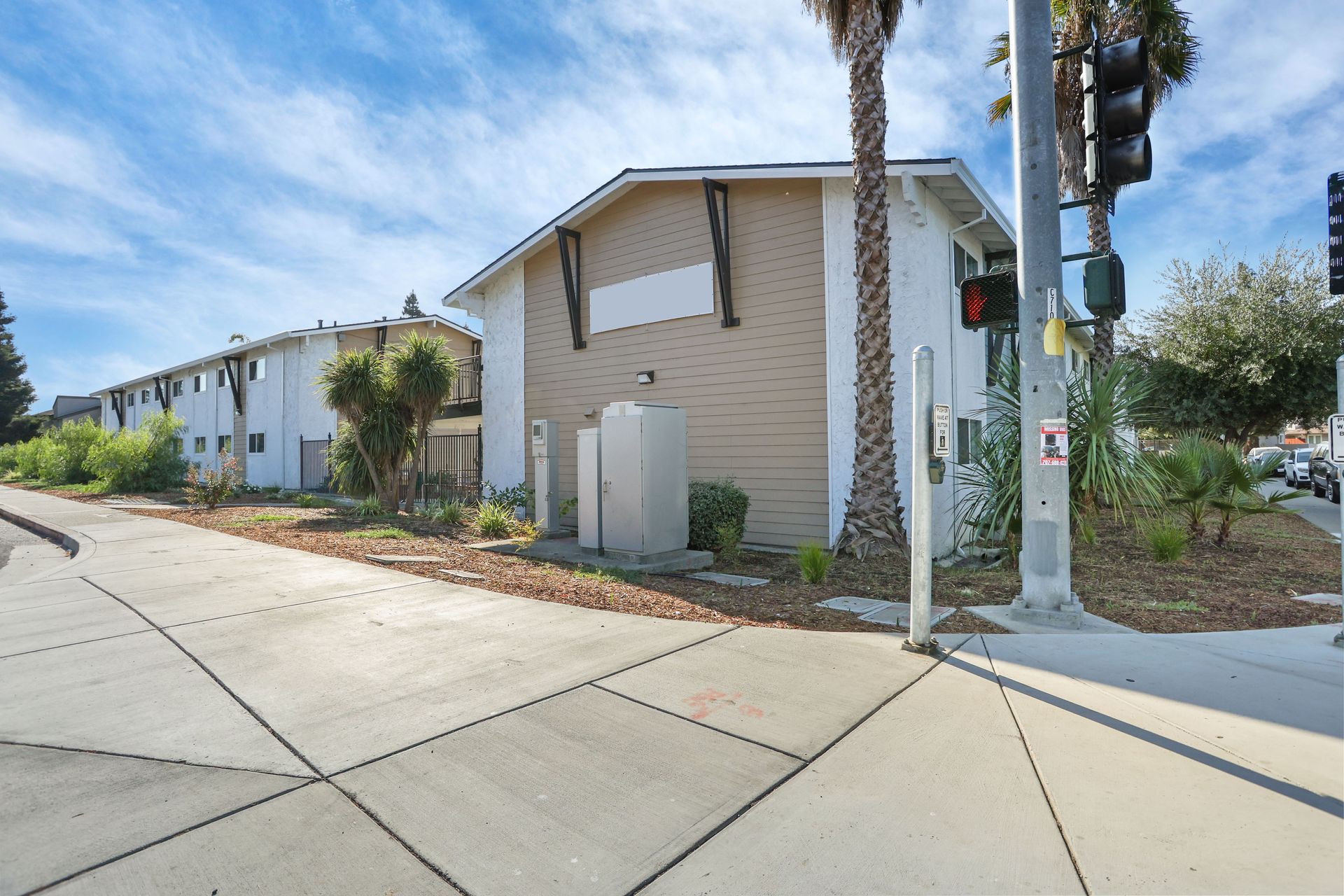 Apartment building corner with palm trees, sidewalk, and utility poles on a sunny day