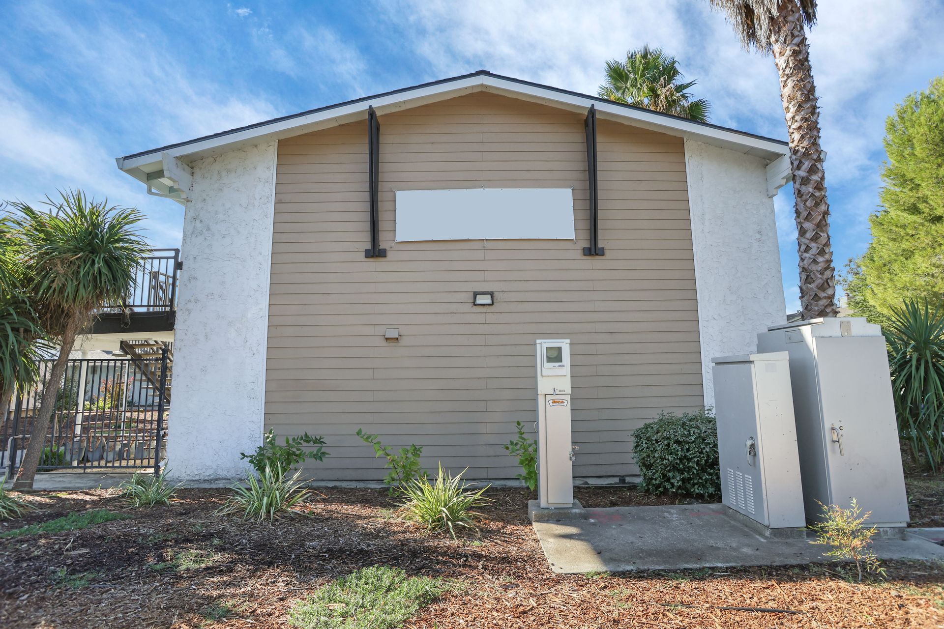 Front view of a beige townhouse with white walls, small shrubs, and a clear blue sky