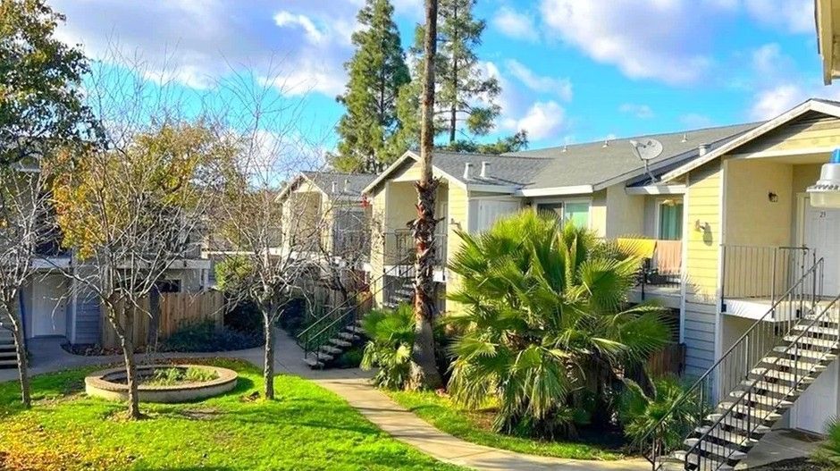 Apartment courtyard with green lawn, palm trees, and stairs beside beige buildings under a blue sky
