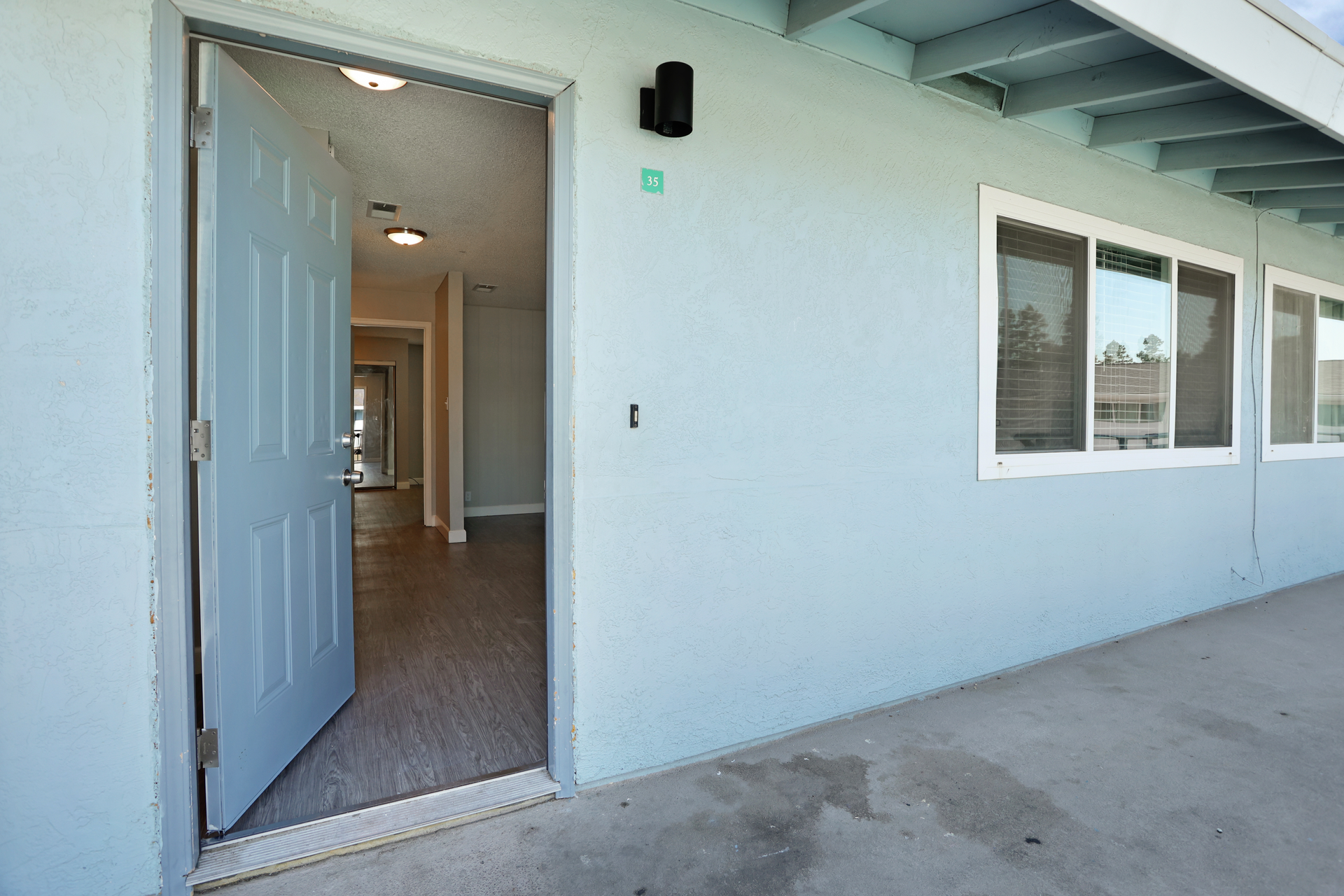 Open front door of a light blue house with windows and a covered porch.